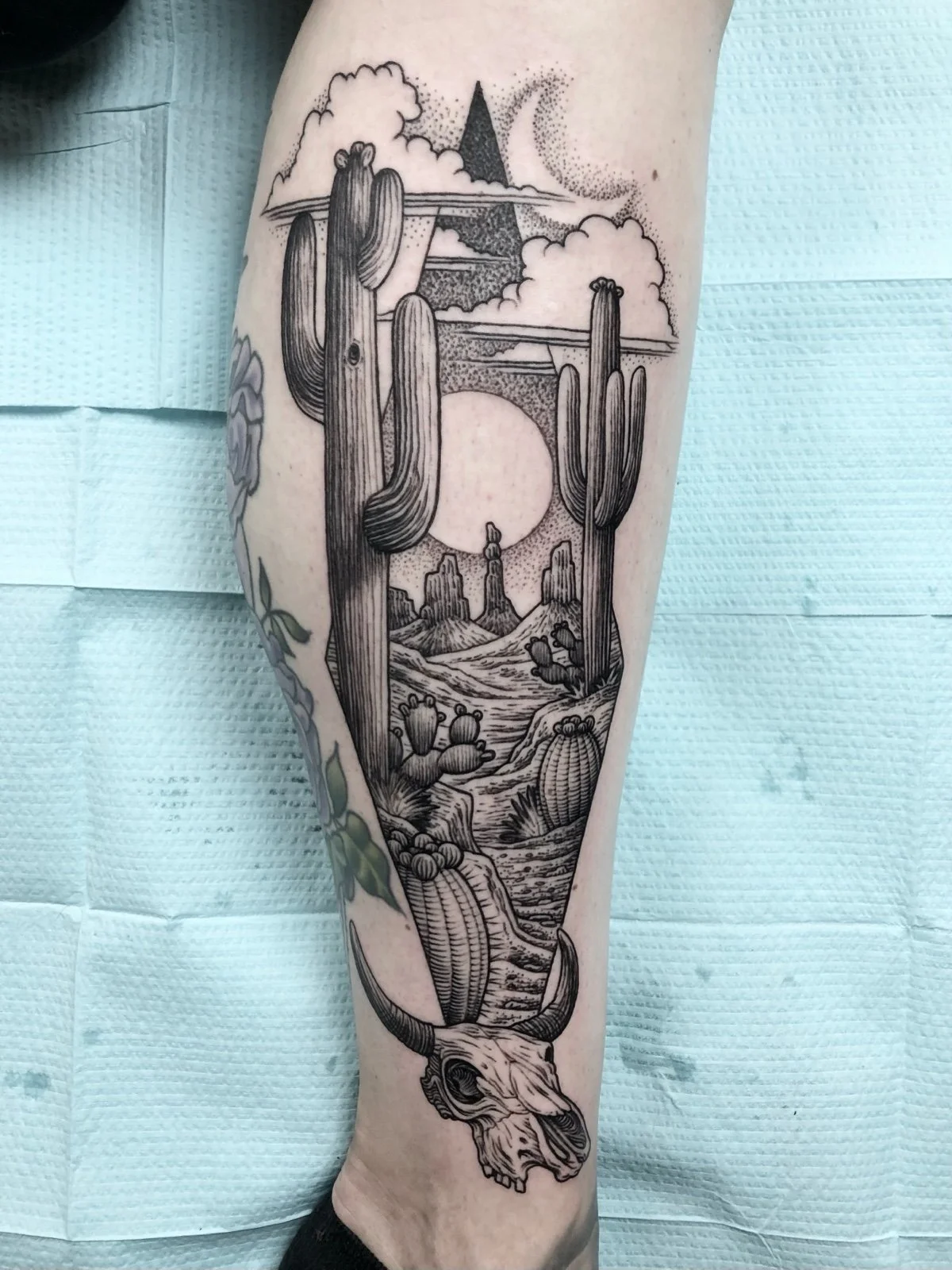 A fine line black and grey southwest desert landscape tattoo, with saguaro cactus and cow skull , created by Seattle tattoo artist Eli Bischof.