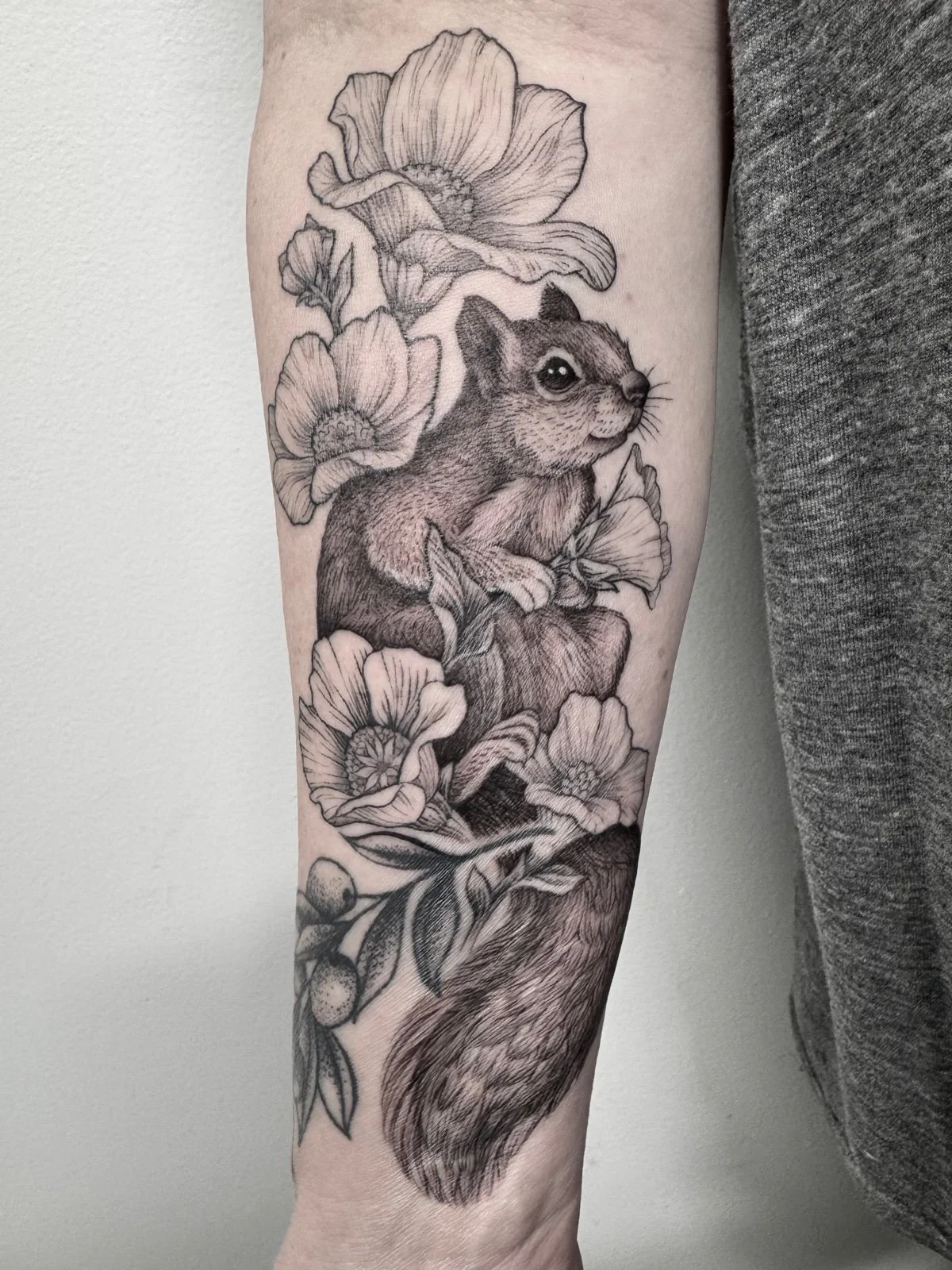 A fine line black and grey illustrative tattoo of a cute squirrel holding a flower, created by Seattle tattoo artist Eli Bischof.