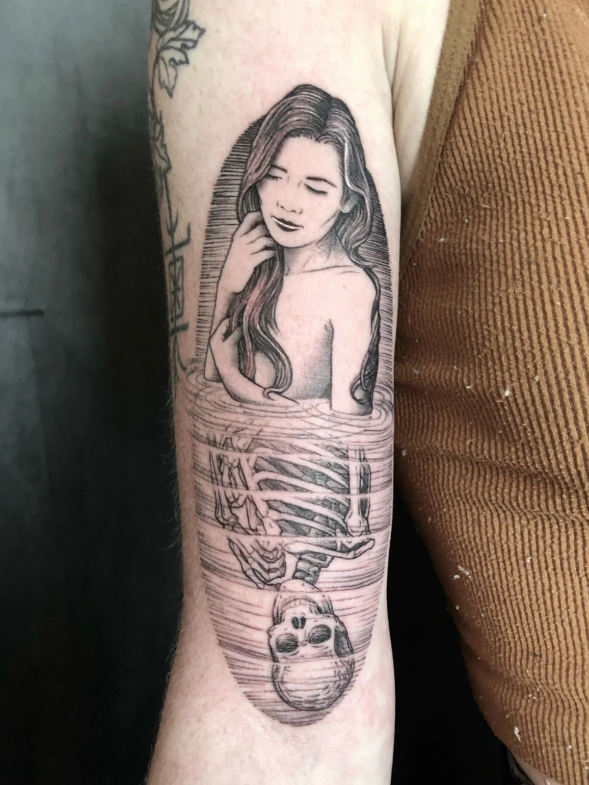 Fine line black and grey surreal tattoo of a woman gazing at her skeleton reflection in water, created by Seattle tattoo artist Eli Bischof.