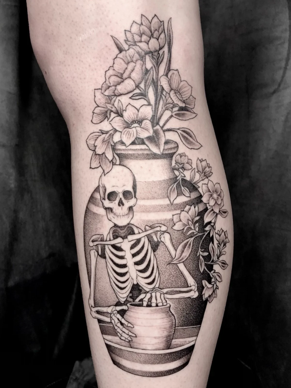 Fine line black and grey skeleton throwing pottery within a ceramic vase with flowers, created by Seattle tattoo artist Eli Bischof.