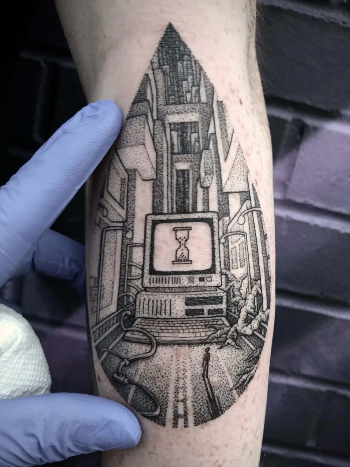 A fine line and black and grey tattoo of a surreal cityscape with a giant vintage computer and a small figure approaching it, created by Seattle tattoo artist Eli Bischof.