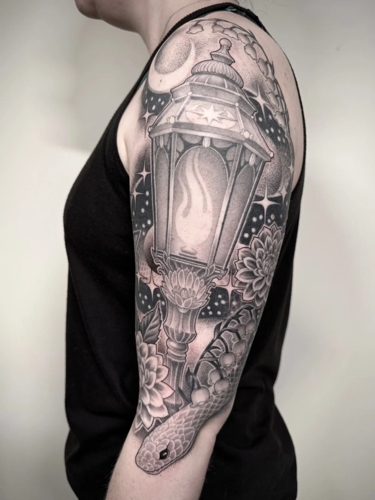 A fine line and black and grey half sleeve tattoo with a witchy theme, including an ornate lamp, celestial elements, a snake, and flowers, created by Seattle tattoo artist Eli Bischof.
