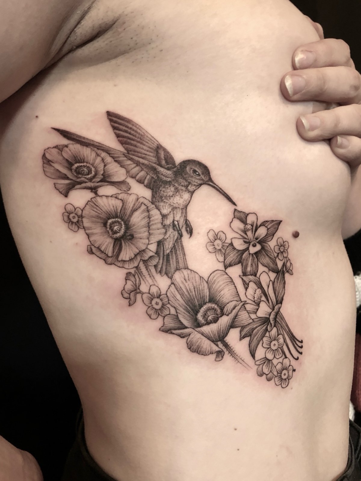 Fine line black and grey tattoo on ribs, with hummingbird and flowers, created by Seattle tattoo artist Eli Bischof