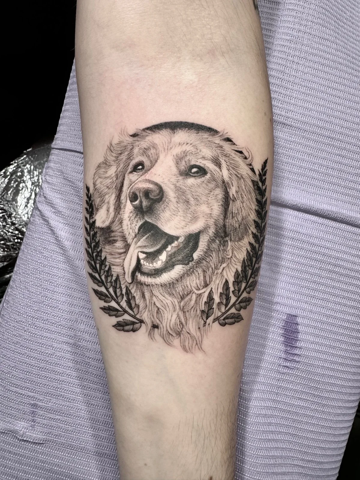 Fine line and black and grey pet portrait tattoo of a golden retriever framed by leaves, created by Seattle tattoo artist Eli Bischof.