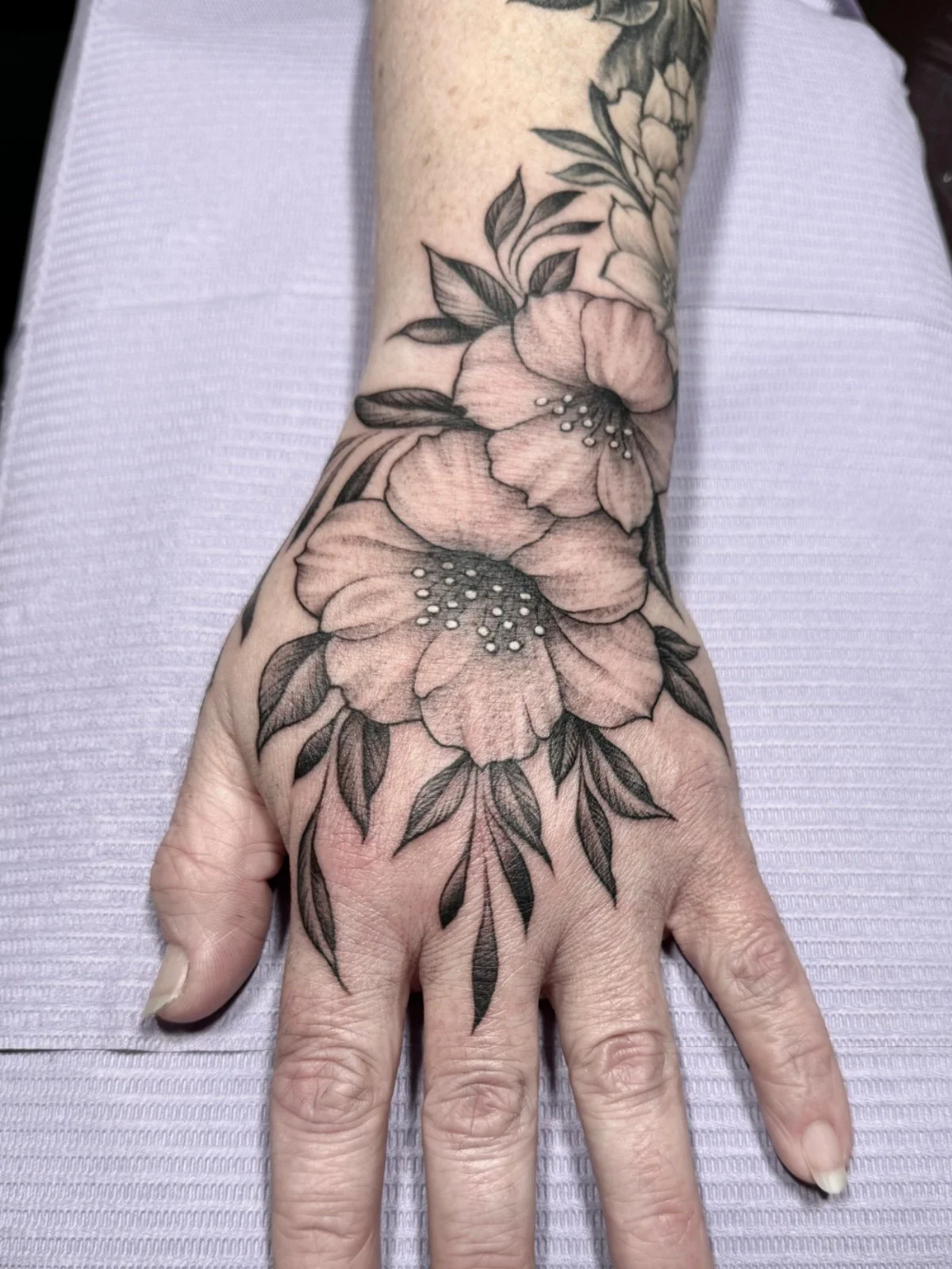 Fine line black and grey hand tattoo with flowers and leaves, designed as companion to other hand tattoo, created by Seattle tattoo artist Eli Bischof