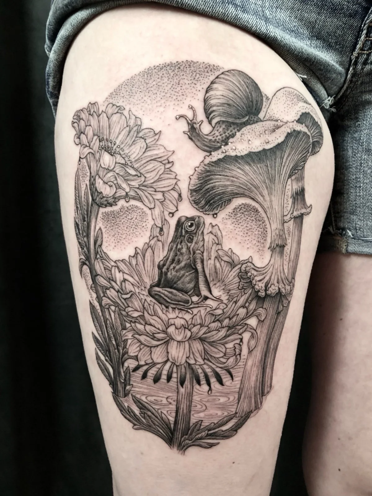 Fine line black and grey skull illusion tattoo, consisting of flowers, mushrooms, with a frog and snail, created by Seattle tattoo artist Eli Bischof.
