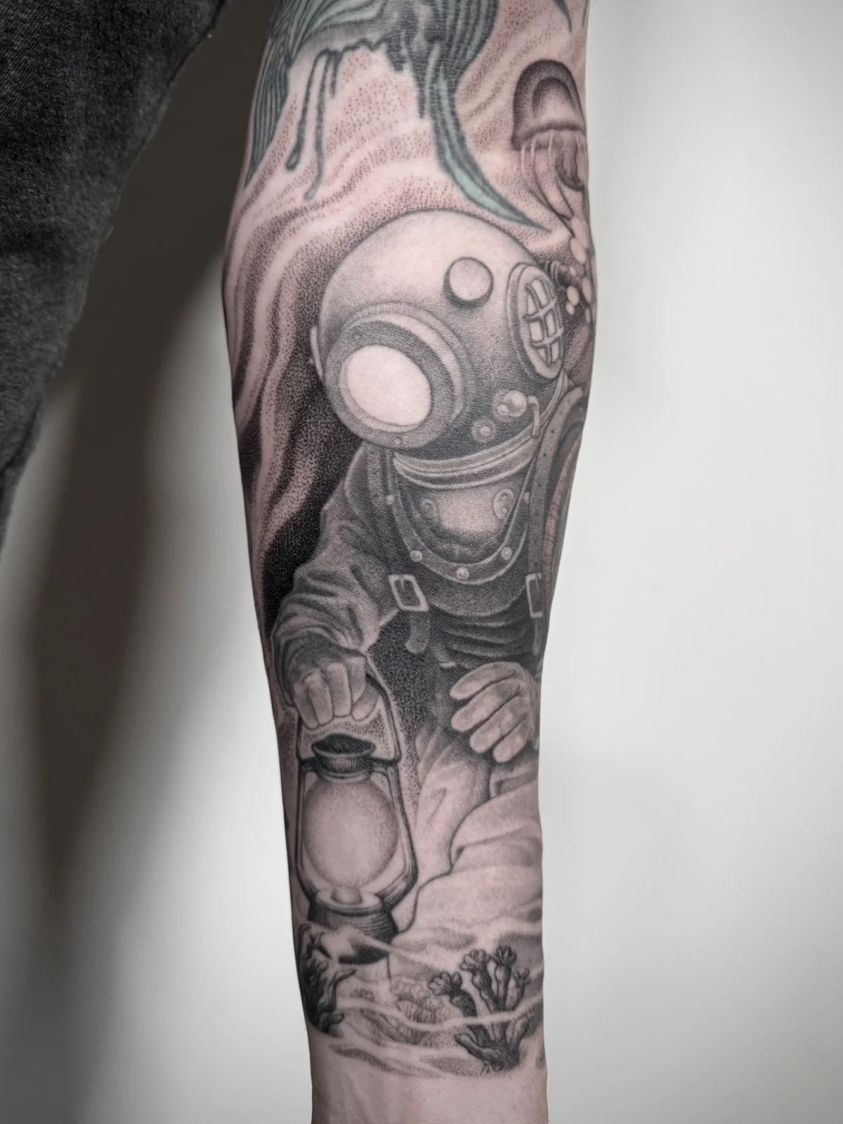 An illustrative black and grey tattoo of a vintage deep sea diver carrying a lantern, created by Seattle tattoo artist Eli Bischof.