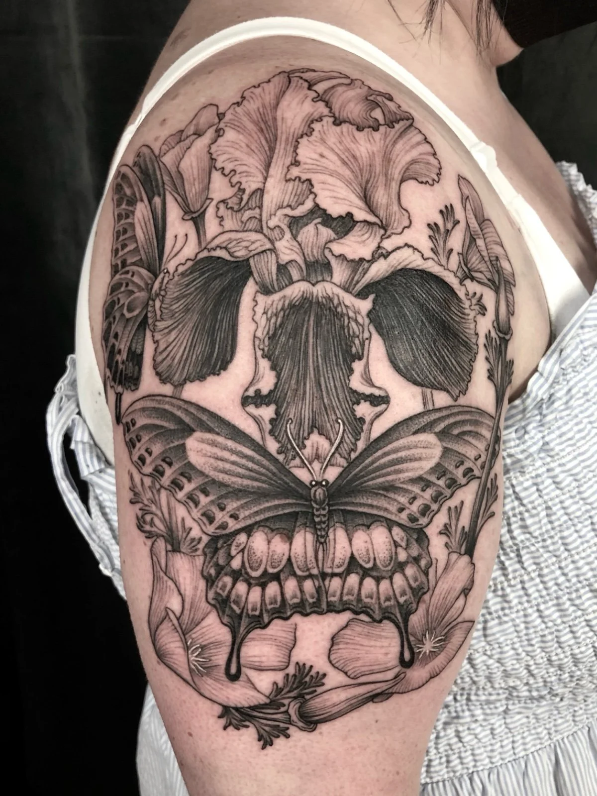 Fine line black and grey skull illusion tattoo, consisting of flowers and butterflies, created by Seattle tattoo artist Eli Bischof.