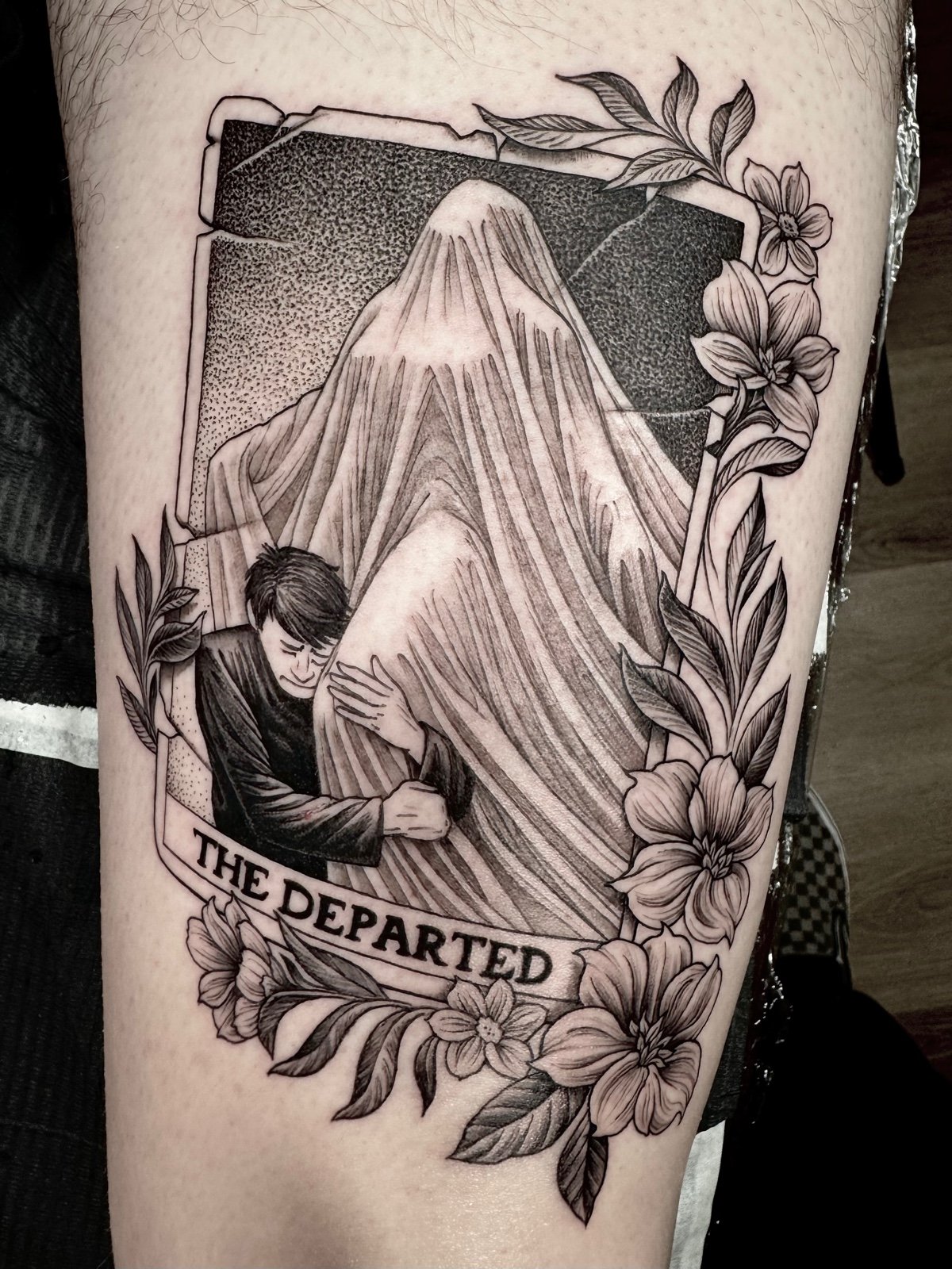 A fine line and black and grey tattoo with dotwork shading of a fictional tarot card of a man clutching the ghostly form of a woman, with floral accents, created by Seattle tattoo artist Eli Bischof.