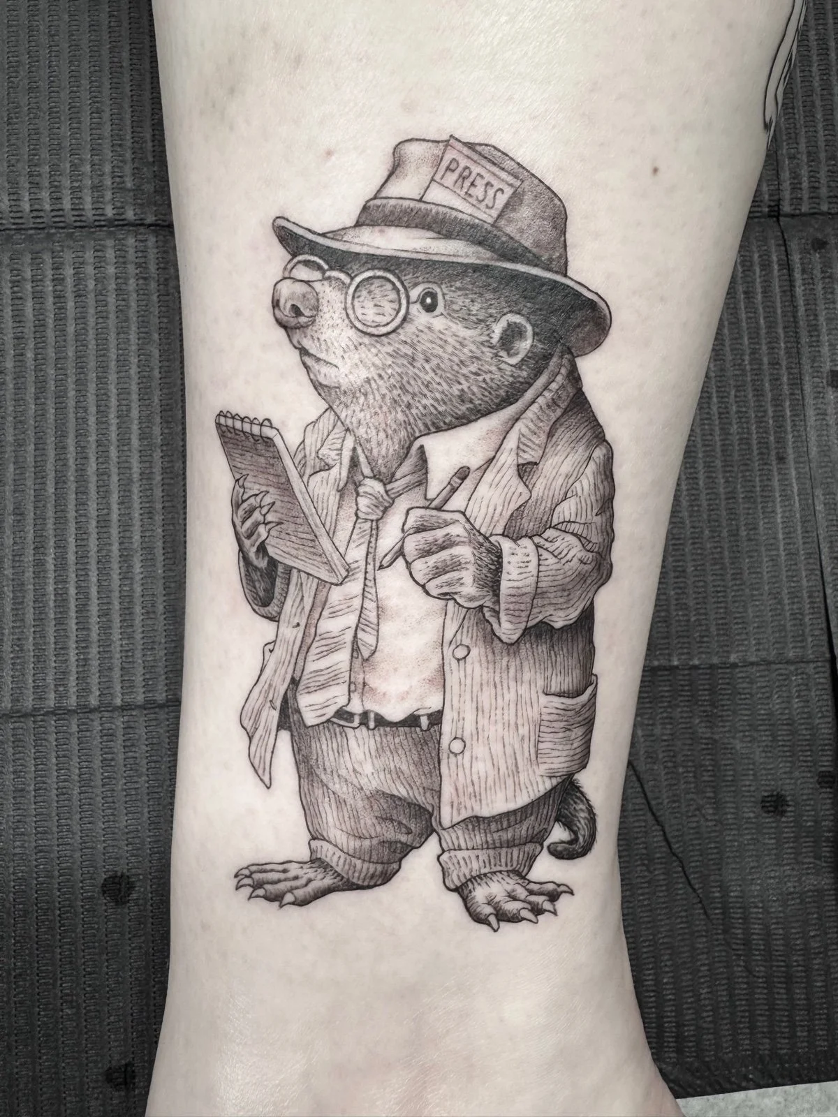 A whimsical fine line and black and grey tattoo of a mole dressed as a reporter and taking notes created by Seattle tattoo artist Eli Bischof.