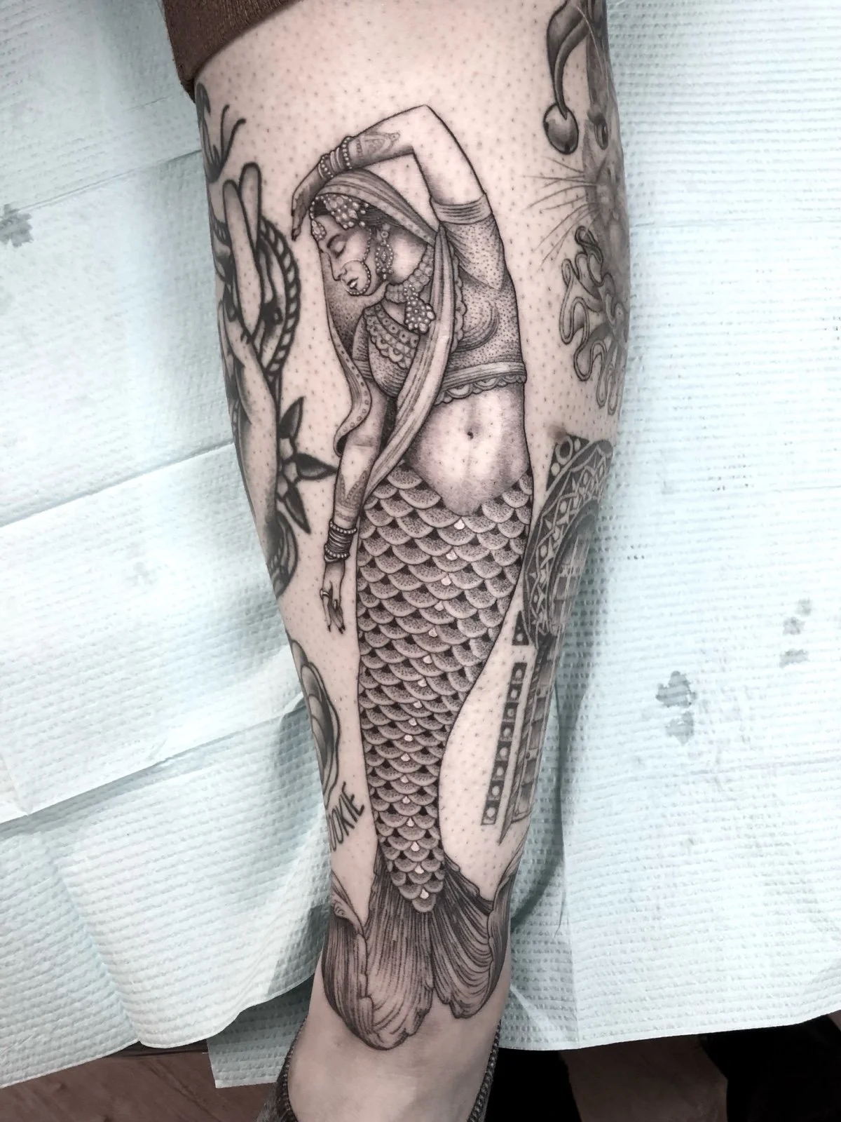 A fine line and black and grey tattoo with dotwork shading, depicting a Pakistani mermaid in an elegant pose, created by Seattle tattoo artist Eli Bischof.