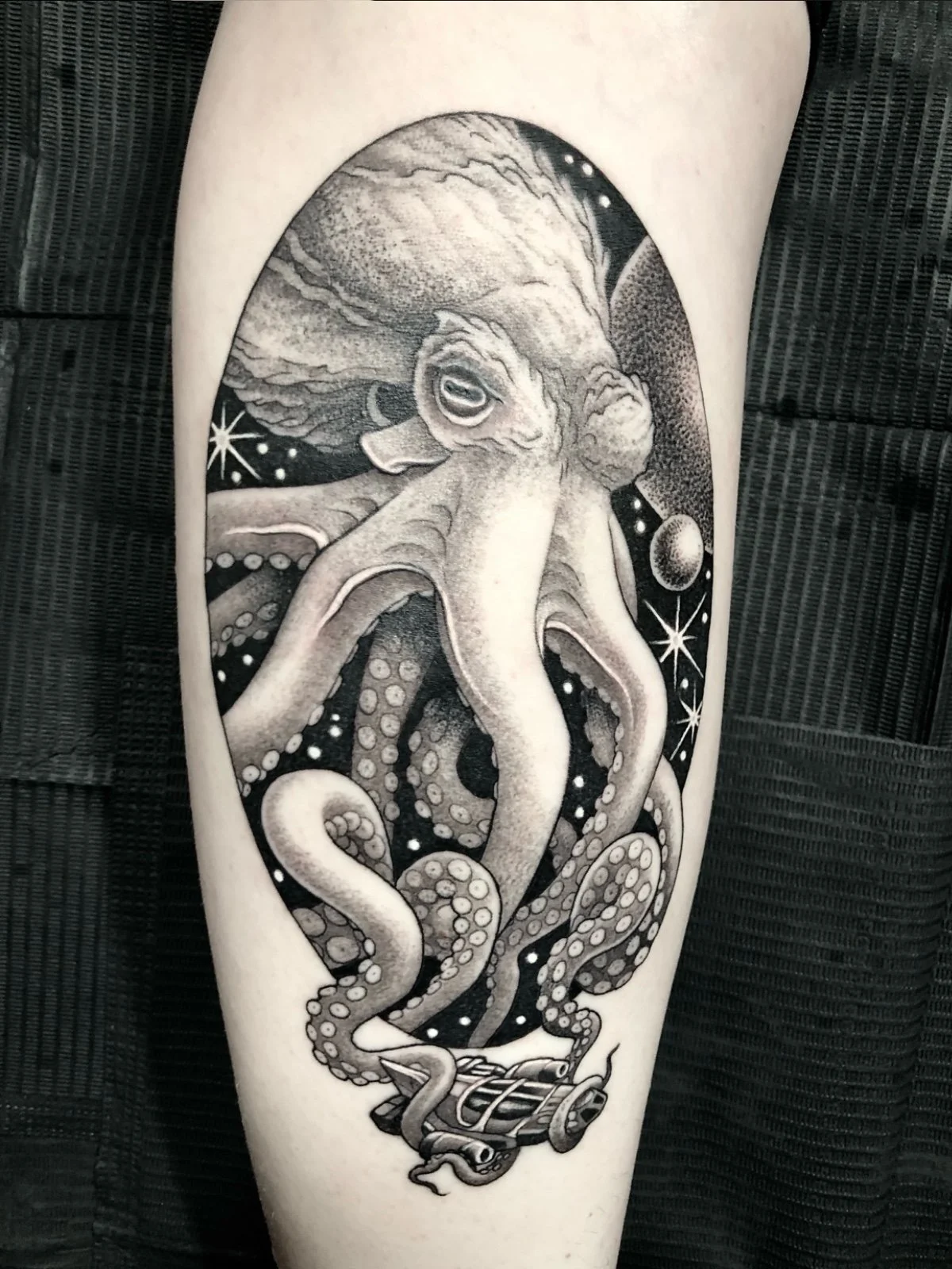 A fine line and black and grey tattoo of an octopus in space, with a spaceship wrapped in its tentacles, created by Seattle tattoo artist Eli Bischof.
