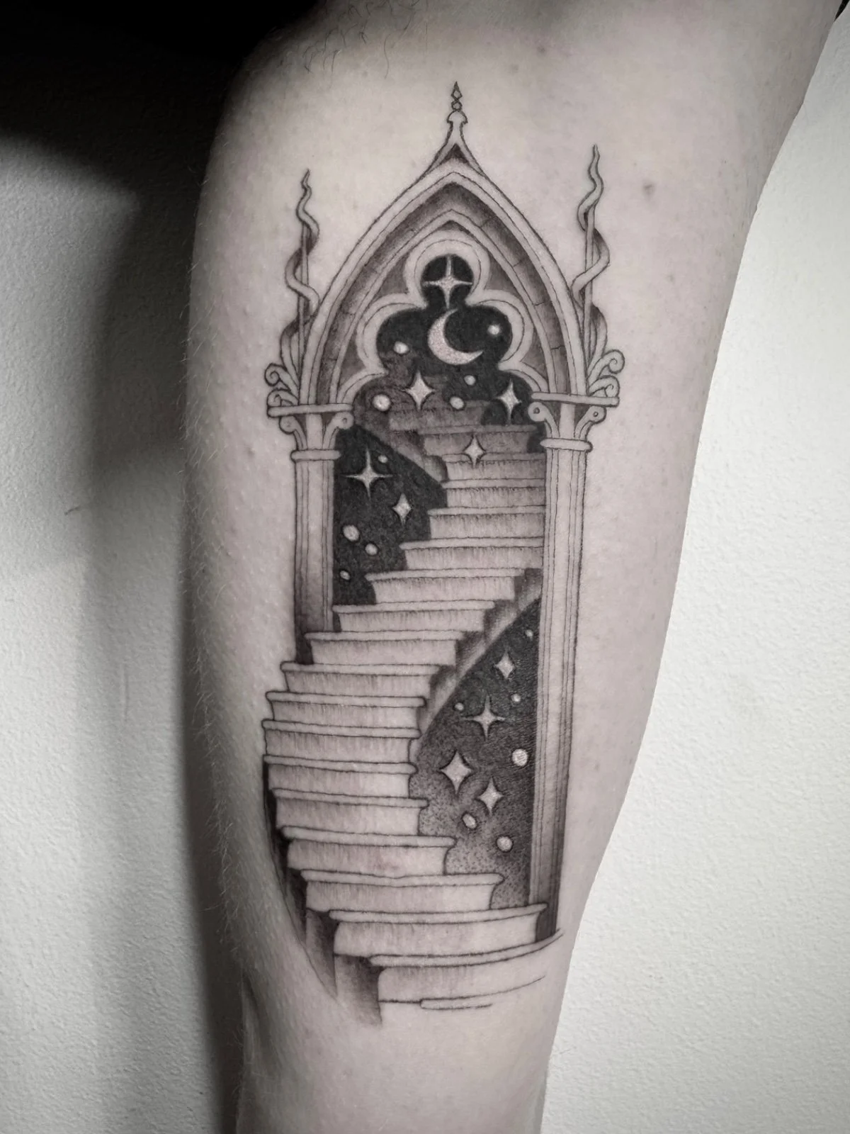 A fine line and black and grey tattoo with dotwork shading, depicting a magical staircase leading through an ornate portal door into stars and space, created by Seattle tattoo artist Eli Bischof.