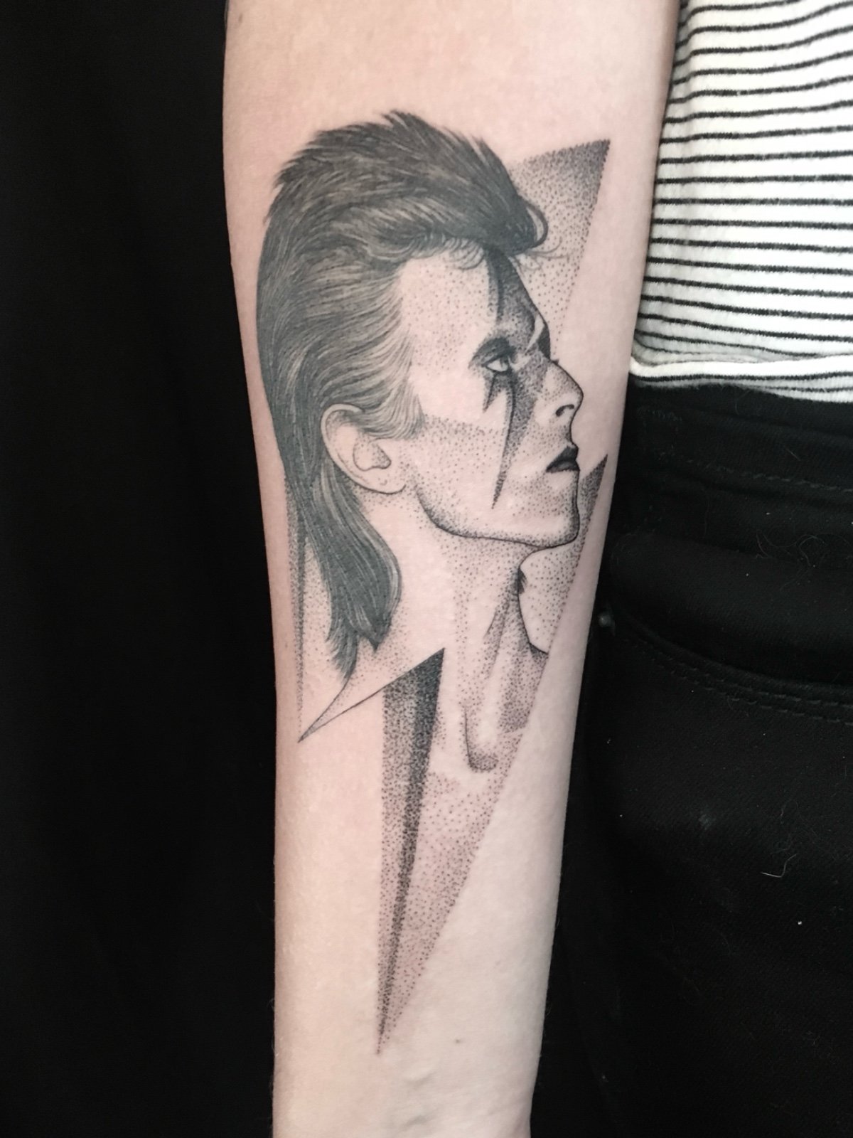 Fine line and black and grey celebrity tattoo portrait of David Bowie as Ziggy Stardust, set within a lightning bolt frame, created by Seattle tattoo artist Eli Bischof.