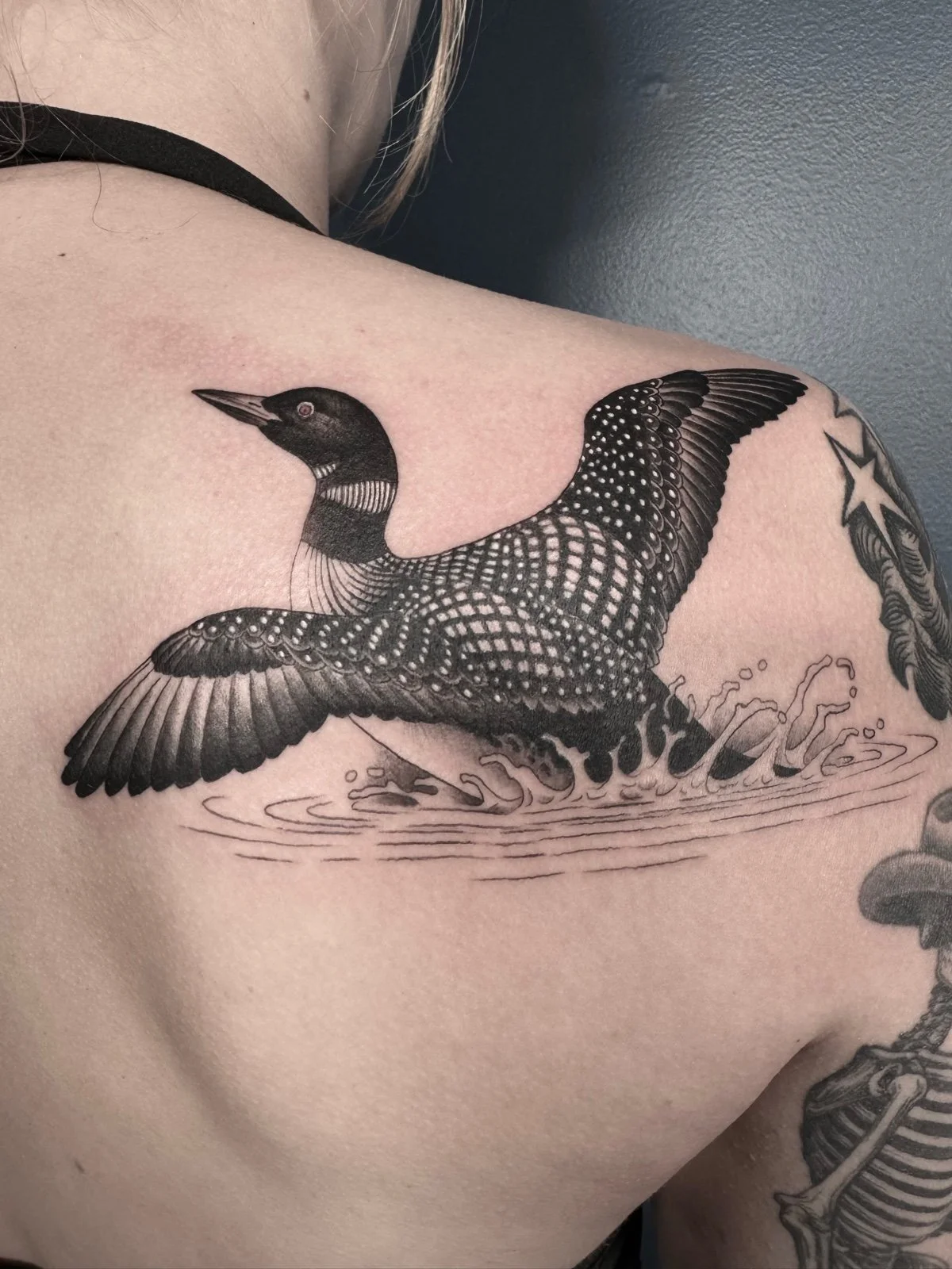 A fine line black and grey tattoo of a loon taking flight from water, created by Seattle tattoo artist Eli Bischof.