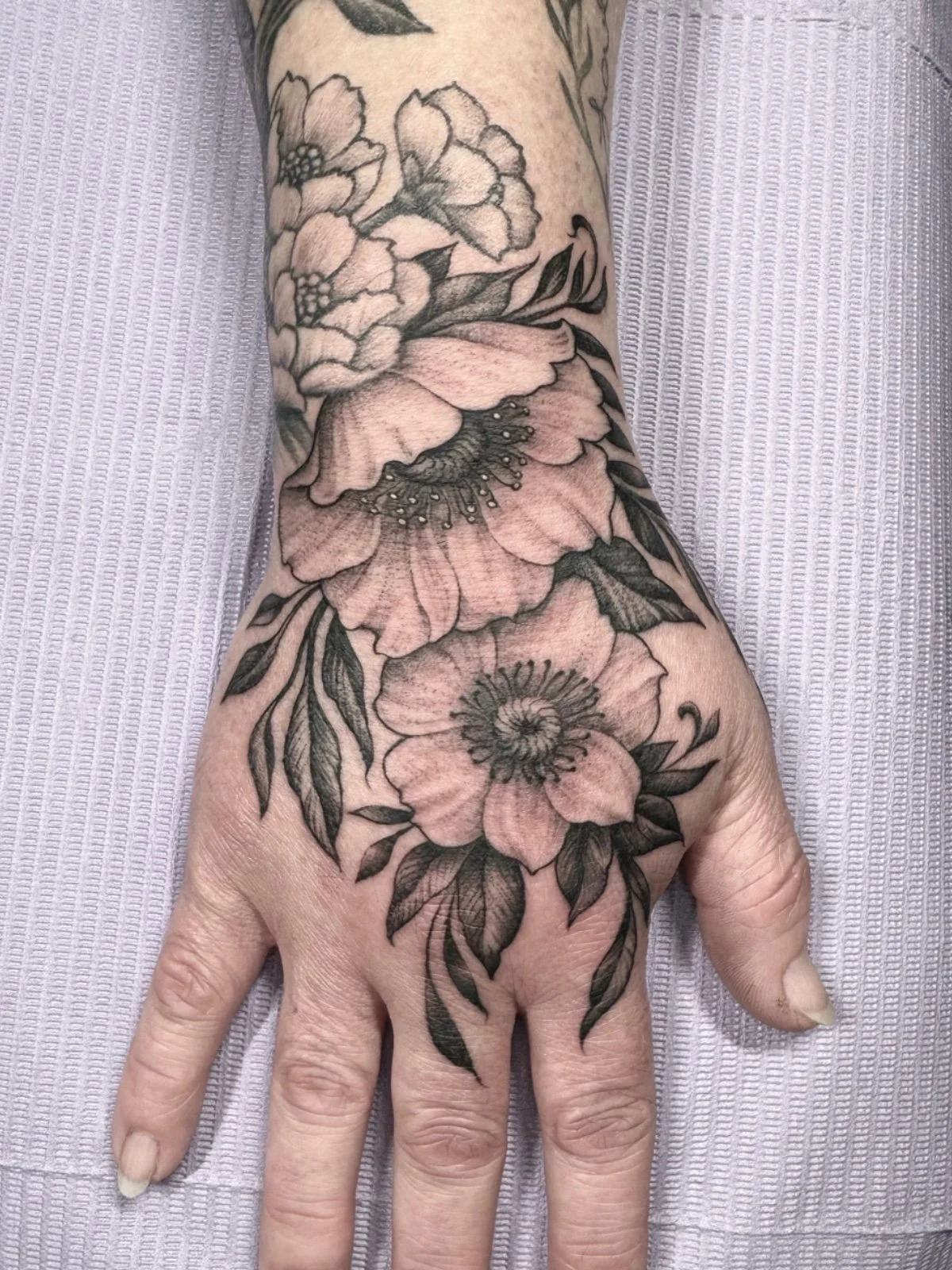 Fine line black and grey hand tattoo with flowers and leaves, designed to compliment other hand tattoo, created by Seattle tattoo artist Eli Bischof