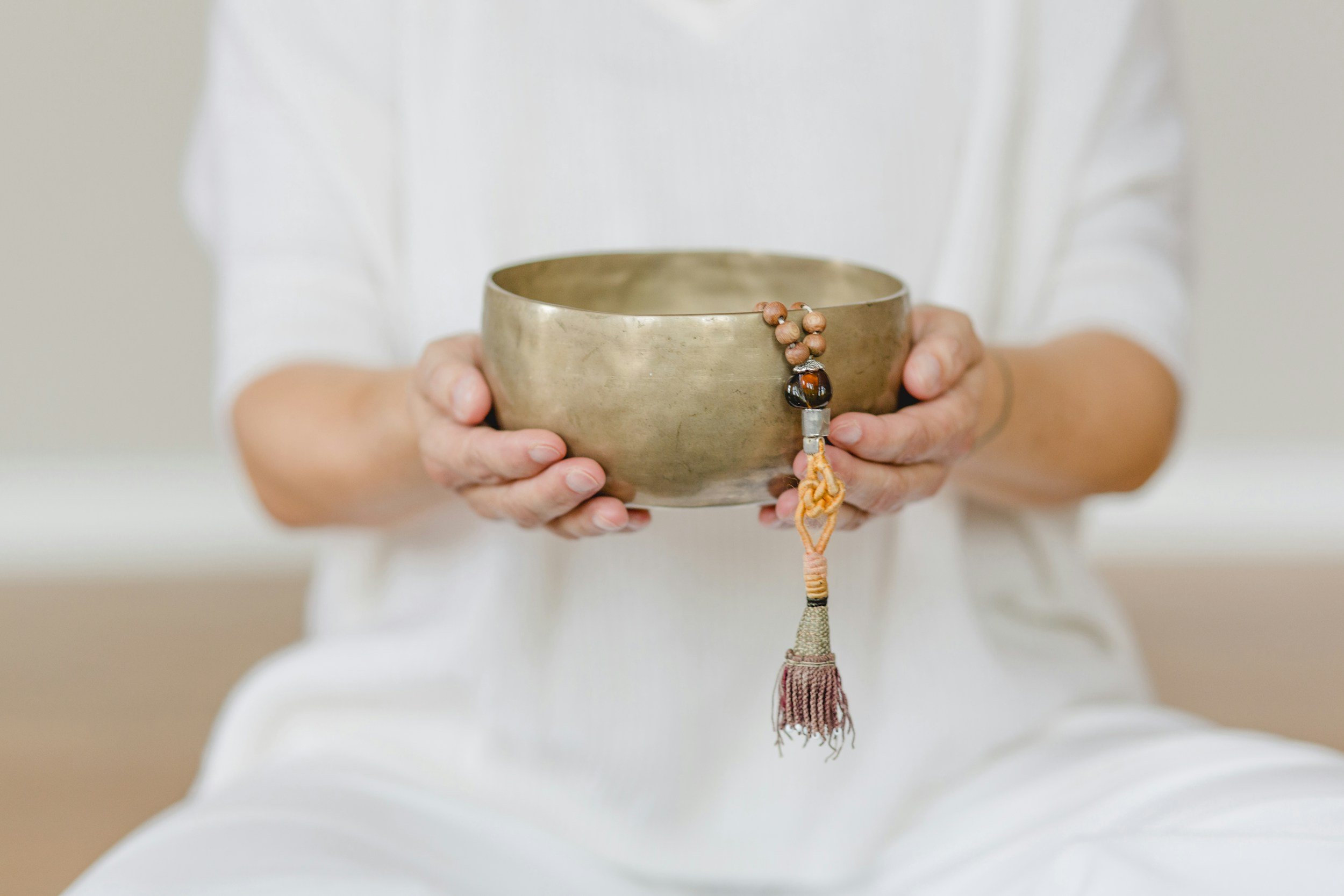 Person holding a bronze singing bowl with a mala prayer bead hanging off its side.