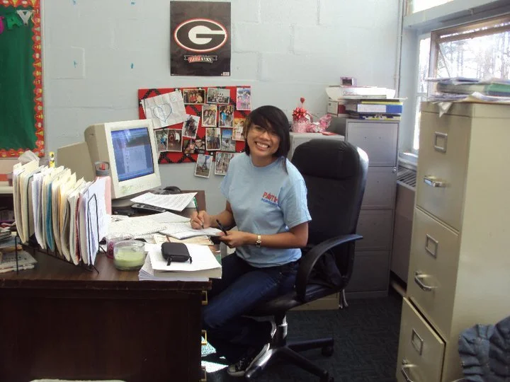 This image shows Toni Rose as a younger educator sitting at their desk.