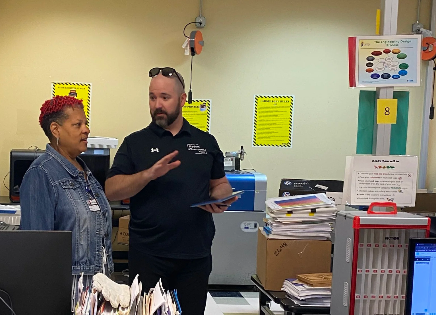 Two educators speak, gesturing to the larger classroom they are standing in.