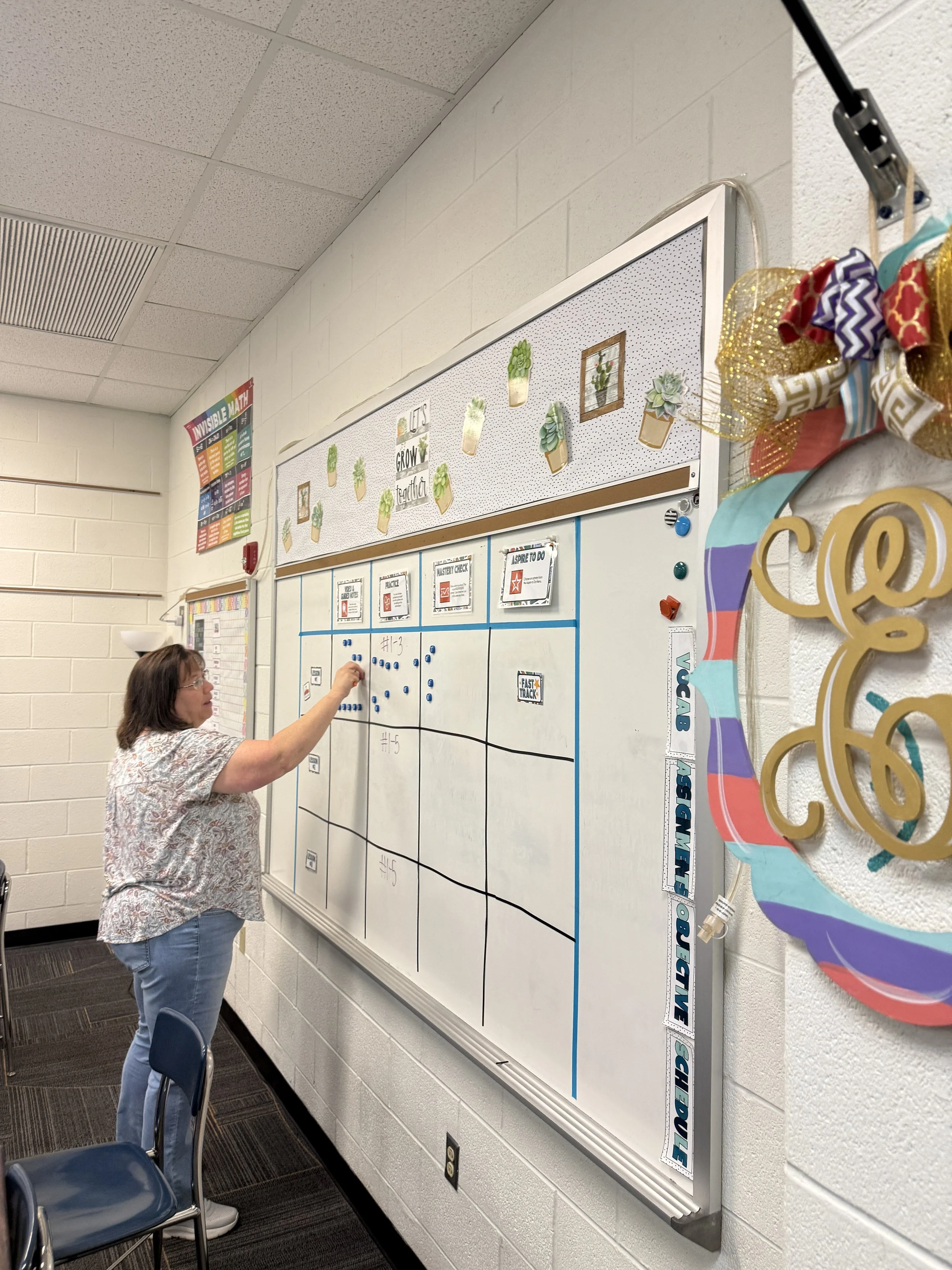 An educator stands at a white board, moving a magnet from one square to another.