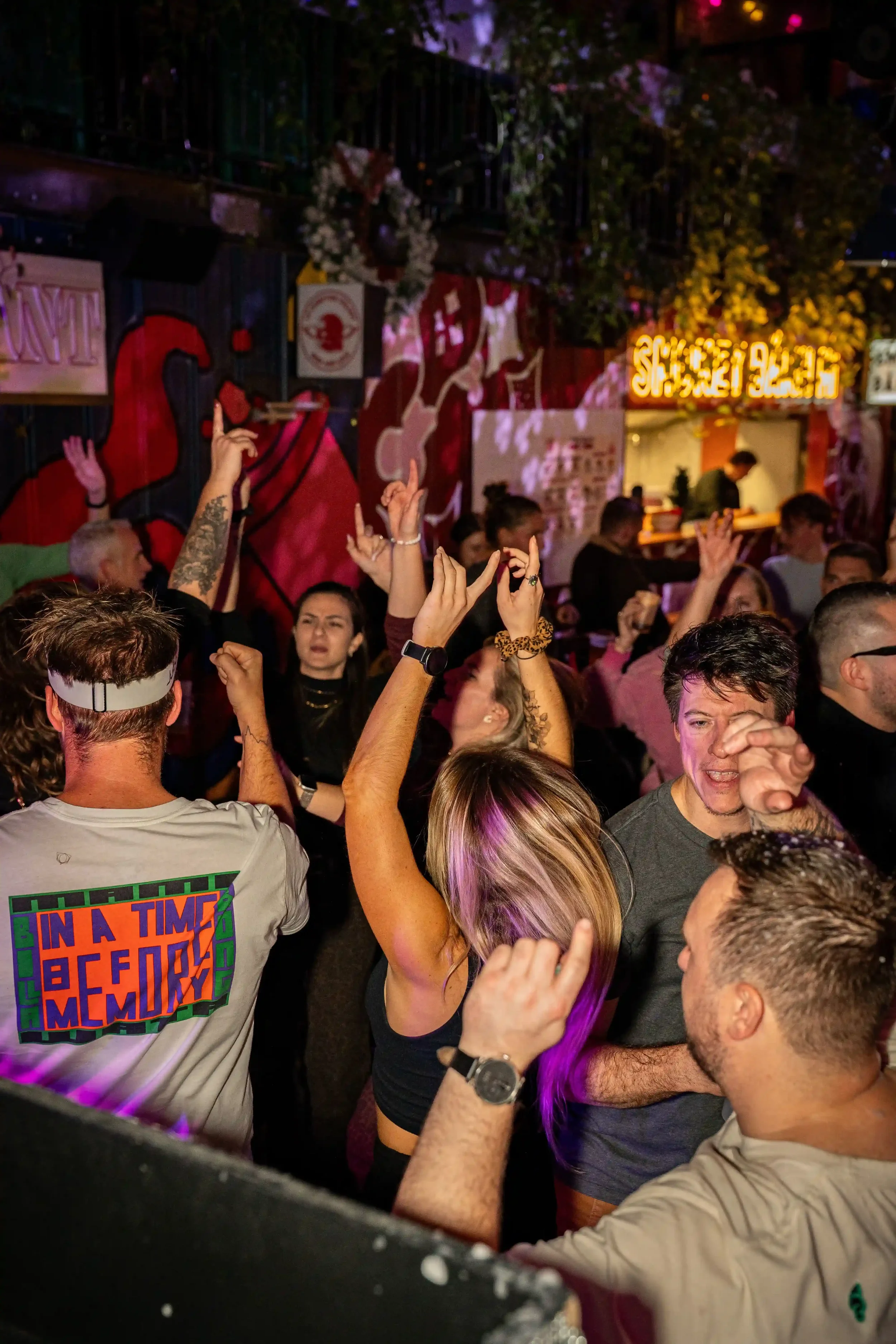 Groupe de personnes dansant et s'amusant dans une ambiance de fête avec des lumières colorées en arrière-plan.