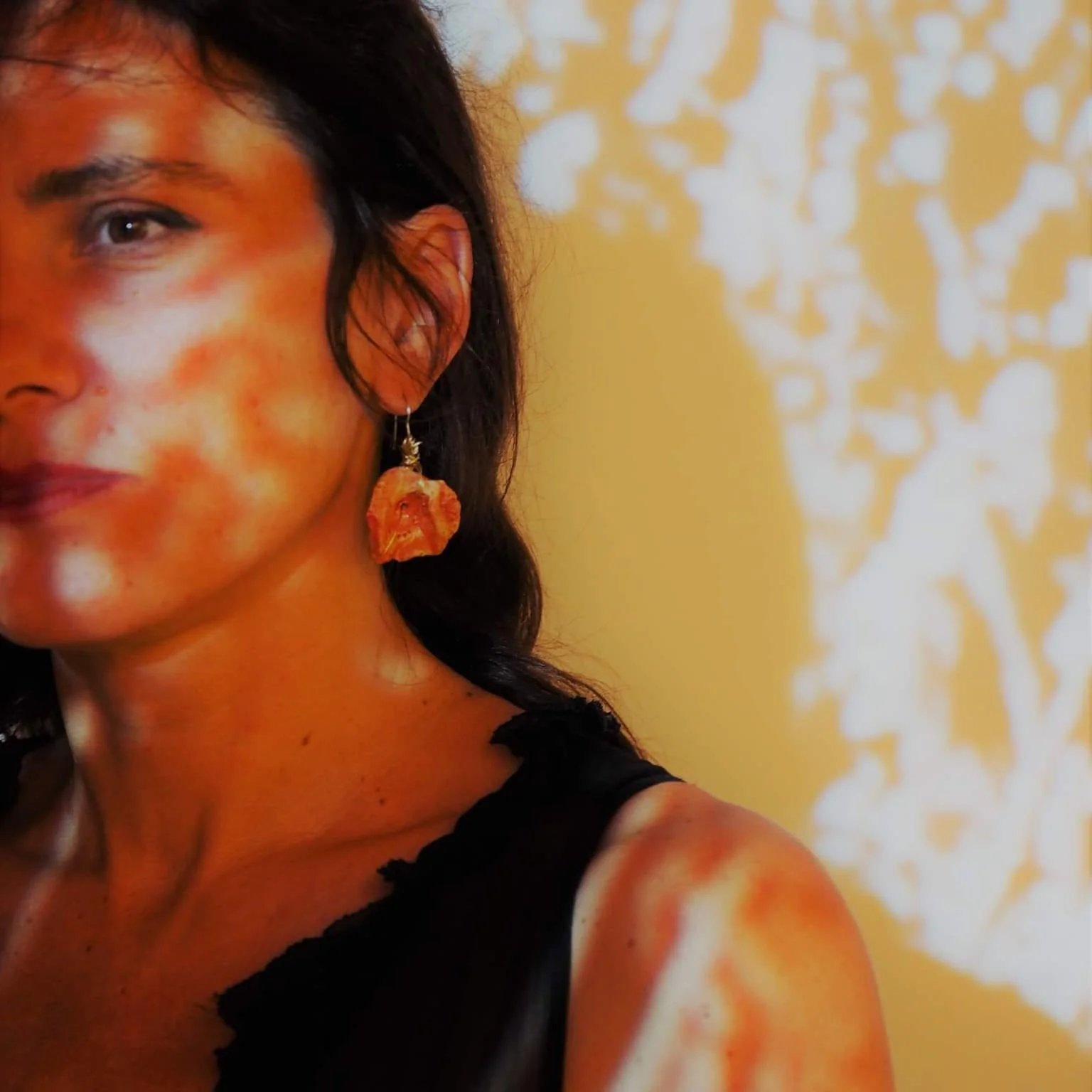 Artistic close-up portrait of Dimitra Kalantzi illuminated by striking patterned orange light and shadow, representing her work at Plastico Gallery.