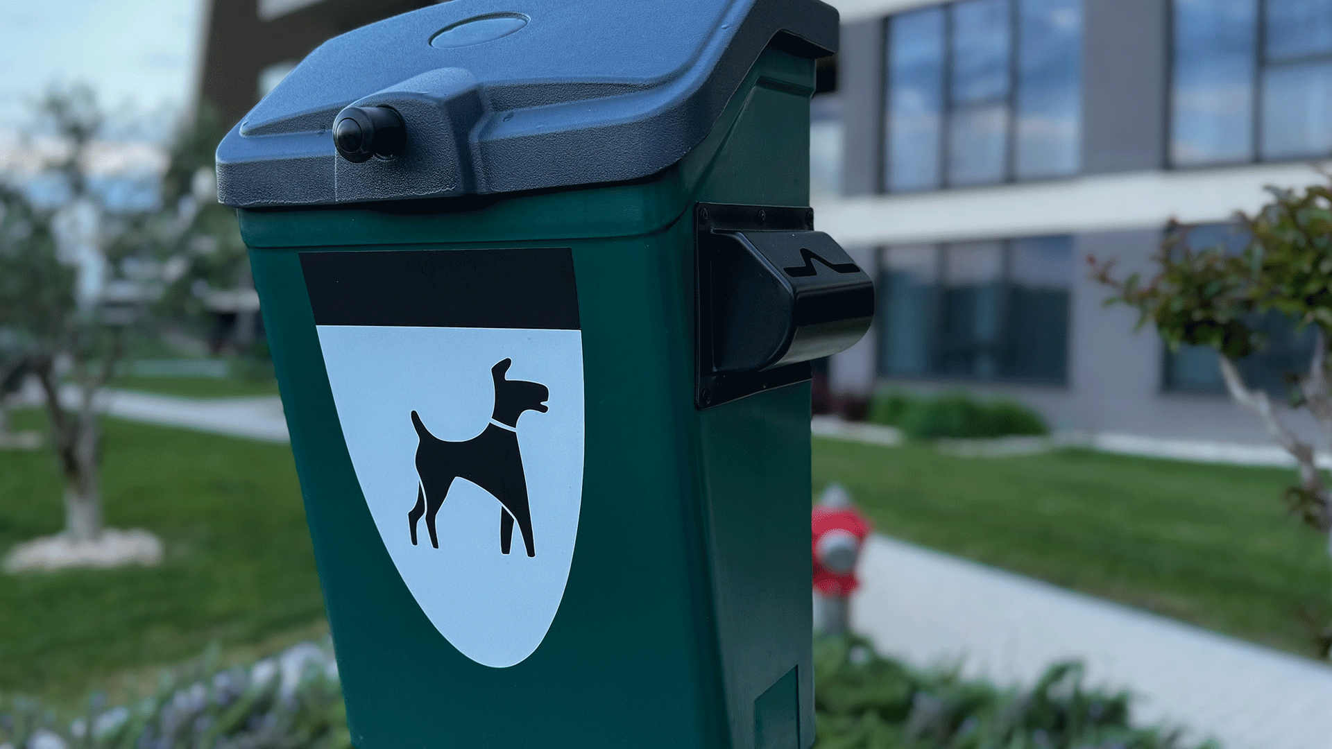 Green bin with stylised imge of  dog on the front. Bckground indicates urban environment.