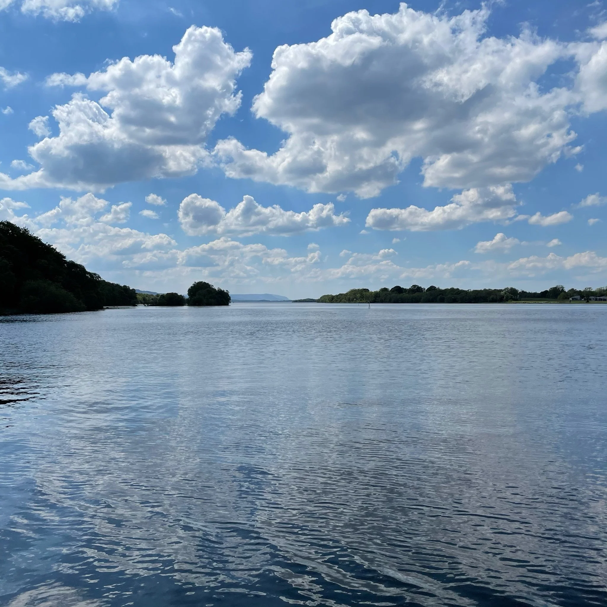 Lough Erne view from Lusty Beg Island Resort, with calm water and bright blue sky with scattered clouds.