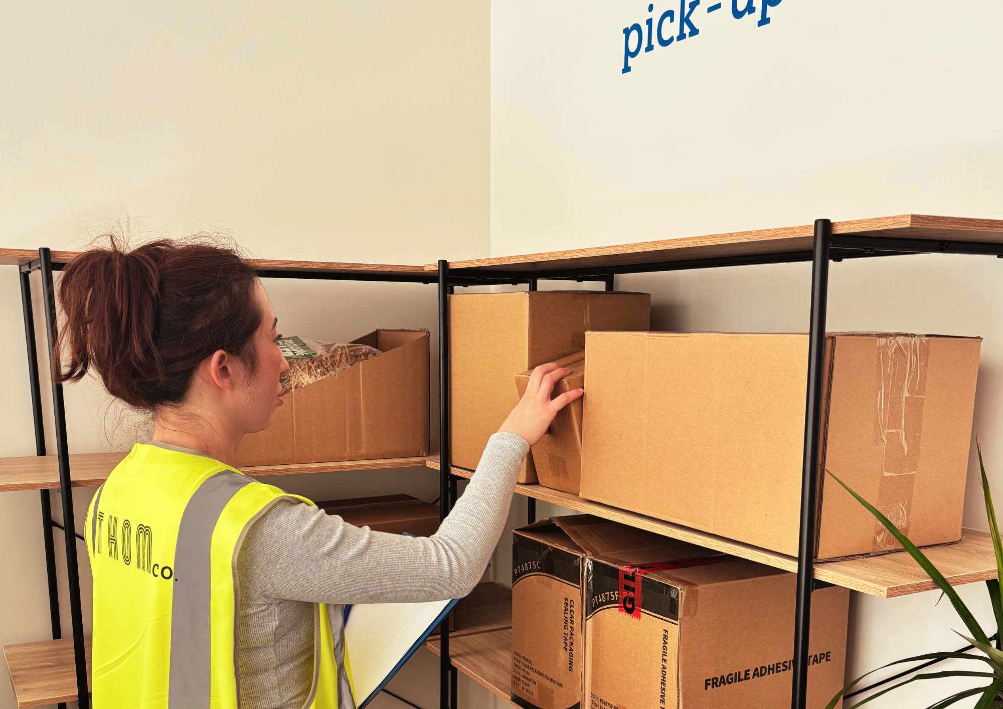 A woman in a yellow safety vest organizing boxes on shelves in a storage room.