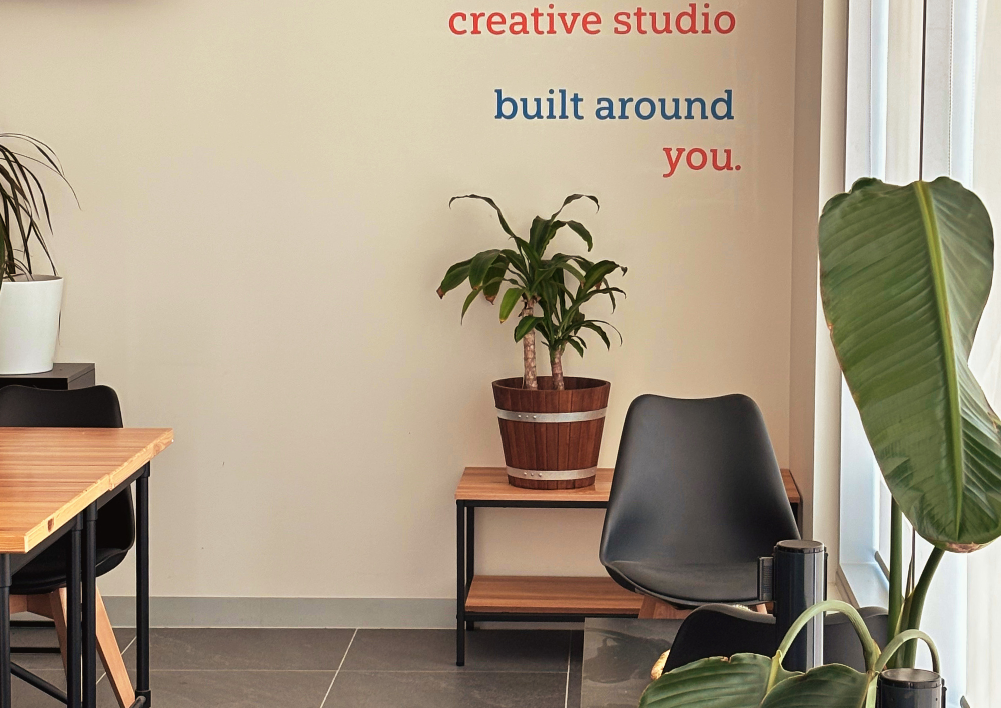 Interior of a creative studio with a wall sign reading 'creative studio built around you', a wooden plant pot with a large leafy plant, and seating arrangements.