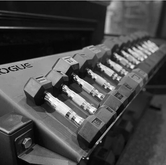 Black and white photo of a set of dumbbells on a rack in a gym.
