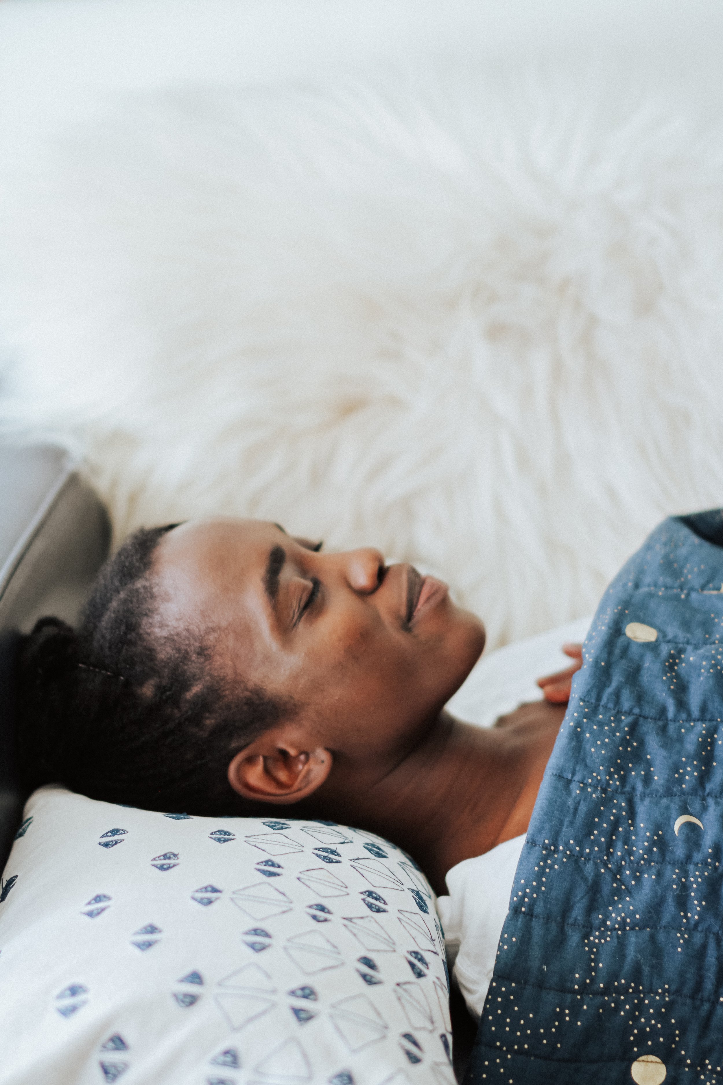 Person sleeping peacefully on a pillow with patterned blue cover and white fluffy background.