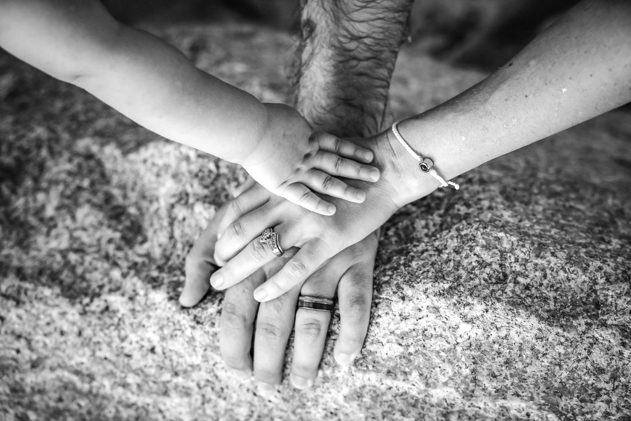 Man, woman and baby putting their hands on top of one another at the beach by sand