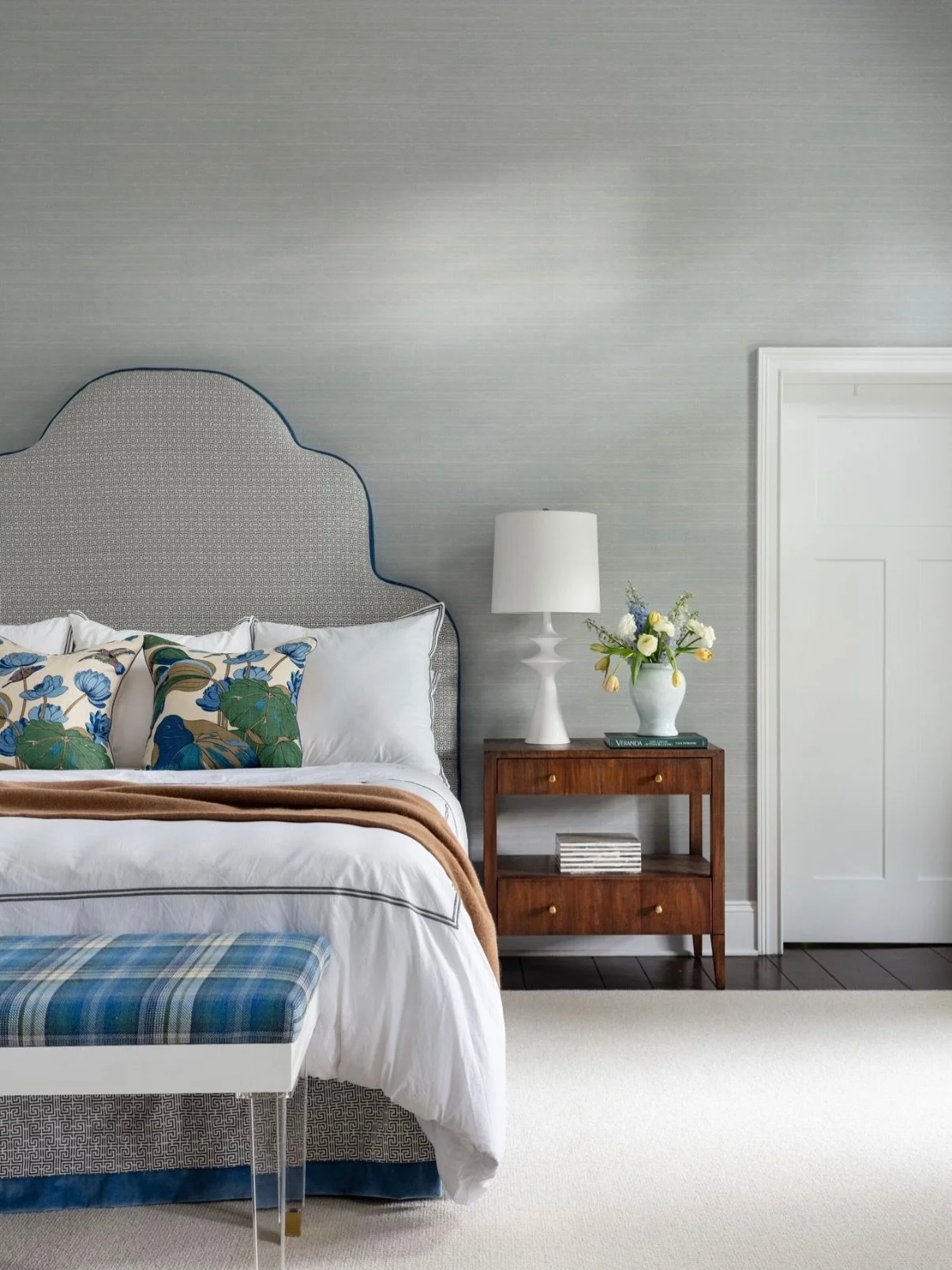 Coastal does not have to mean casual. I love giving it a tailored point of view. Here, watery blue grasscloth wraps the room in a sense of calm, while a custom wave headboard quietly nods to the sea. A tartan wool covered bench (with acrylic legs), b