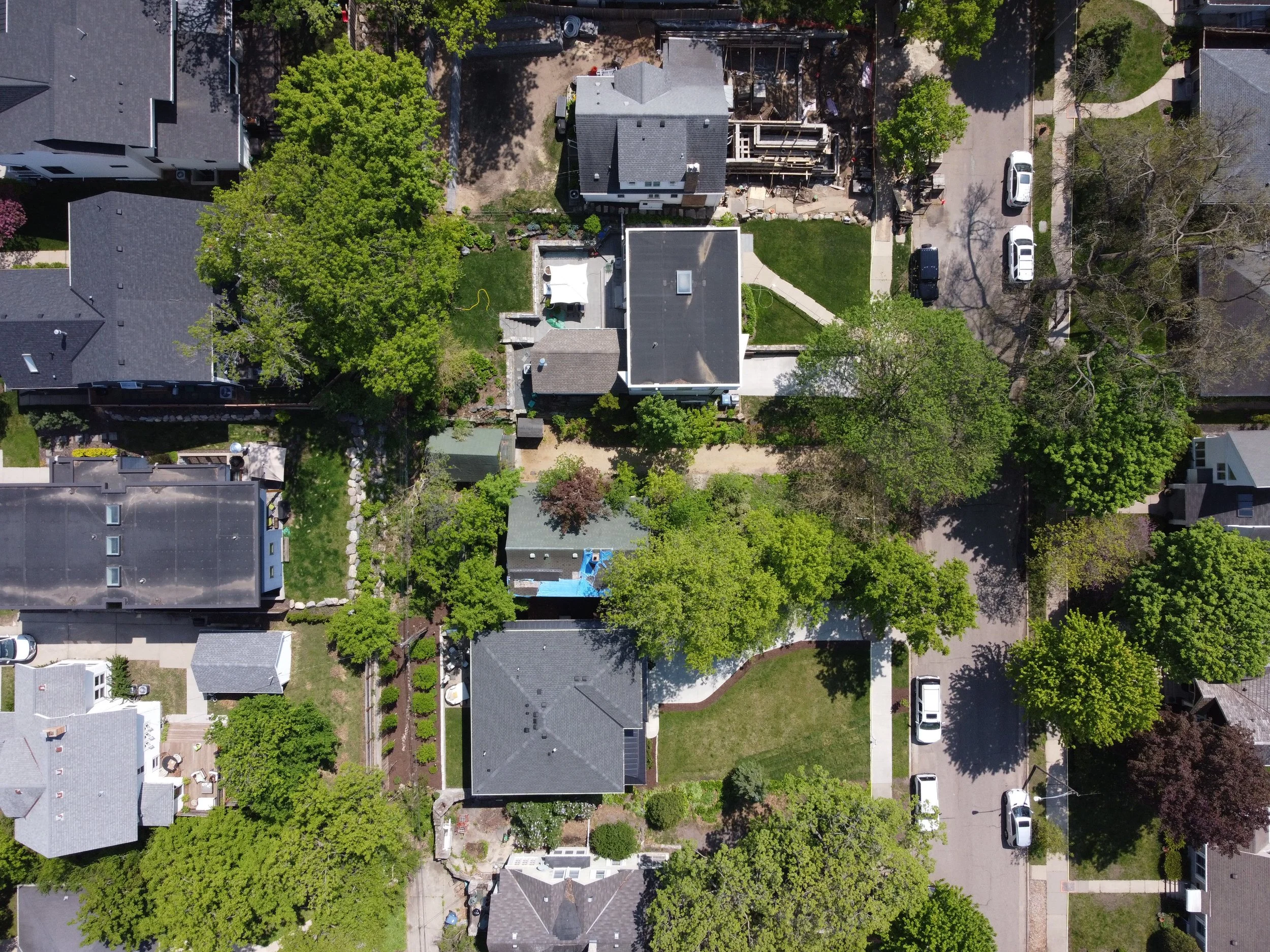 Aerial view of a residential neighborhood with multiple houses, trees, and parked cars along the streets.