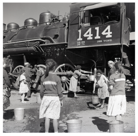 Children getting hot water from a large steam locomotive with the number 1414 in outdoor setting.