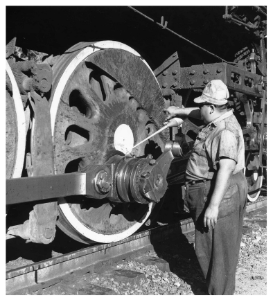 A man in work clothes and a hat oiling the wheel of a large steam locomotive.