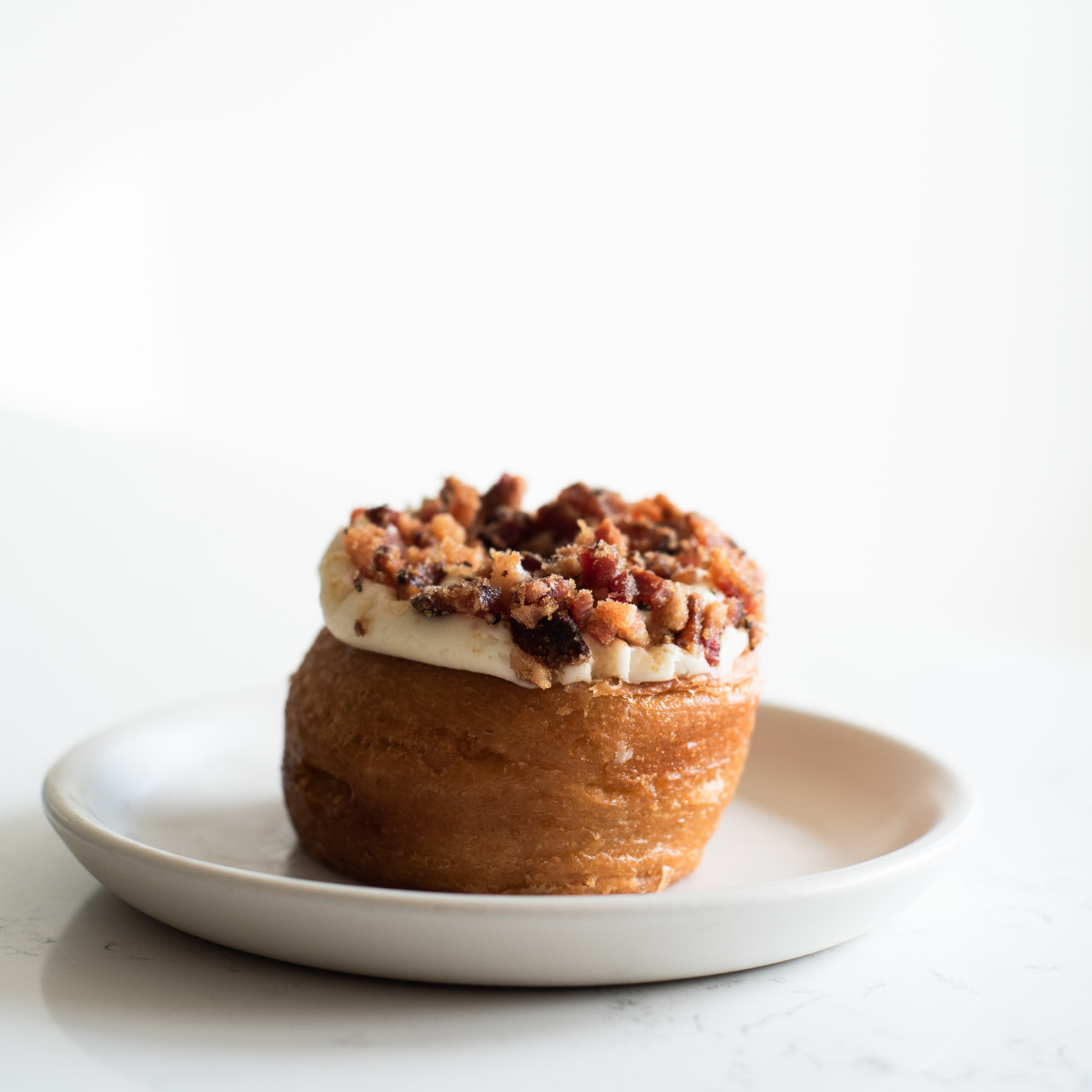 Close-up of a gourmet pastry topped with white icing and a generous sprinkle of crispy bacon bits..png