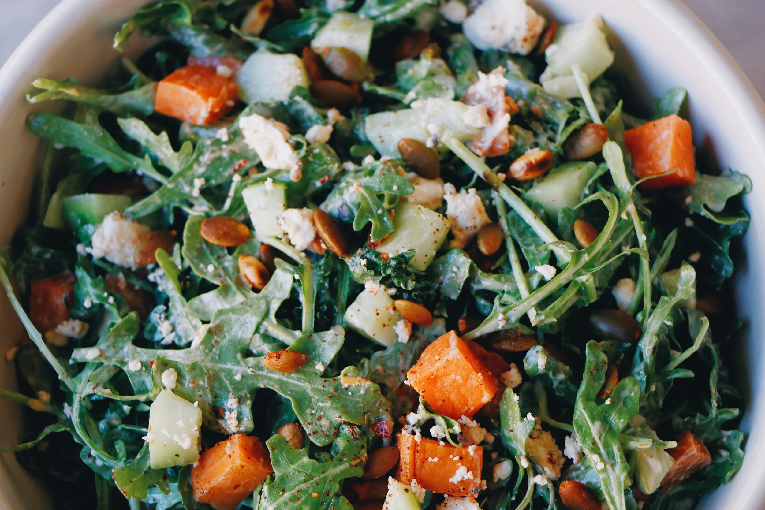 Close-up of a vibrant kale salad with arugula, roasted sweet potatoes, and crunchy seeds, an "All Kale Caesar" salad option..jpg