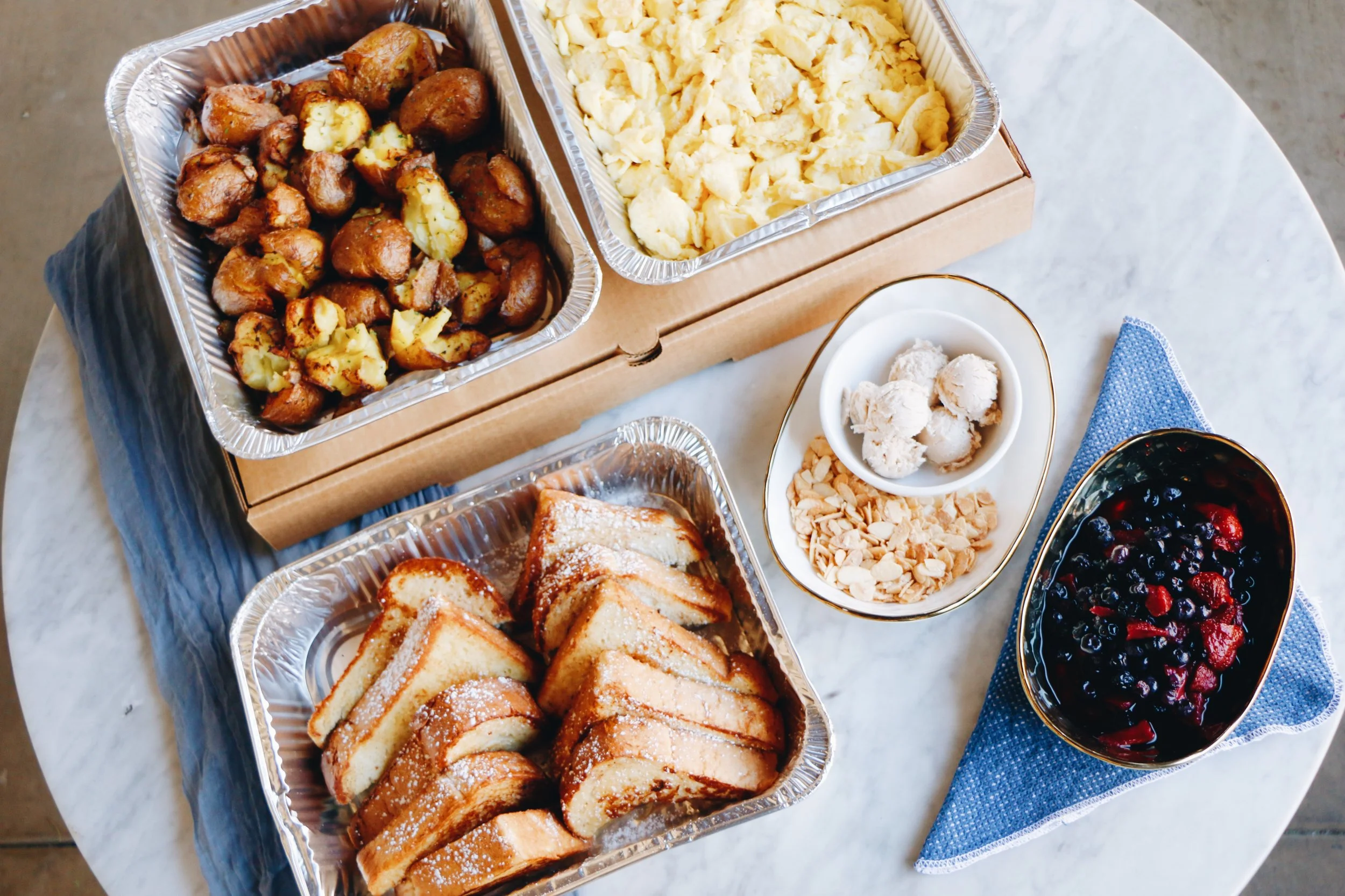 Catering trays filled with roasted breakfast potatoes and French toast, accompanied by small bowls of butter and fresh berry compote..jpg