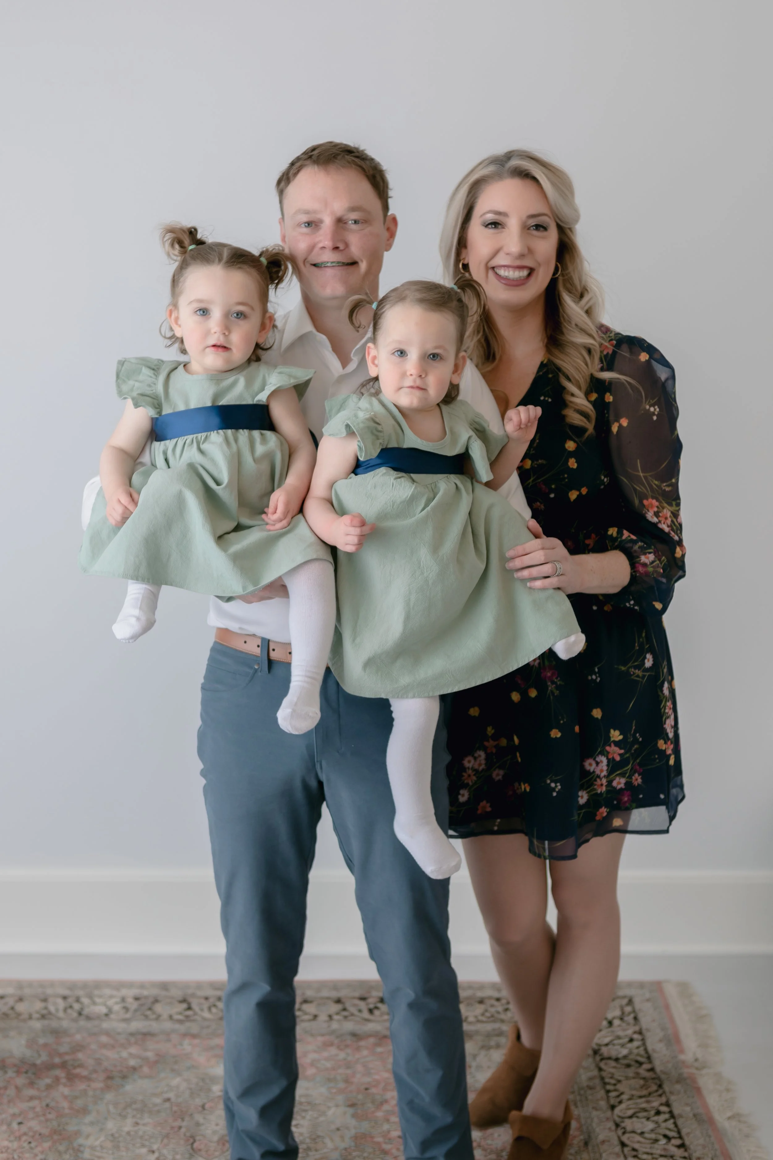 Family portrait with two adults and twin toddlers in matching dresses.