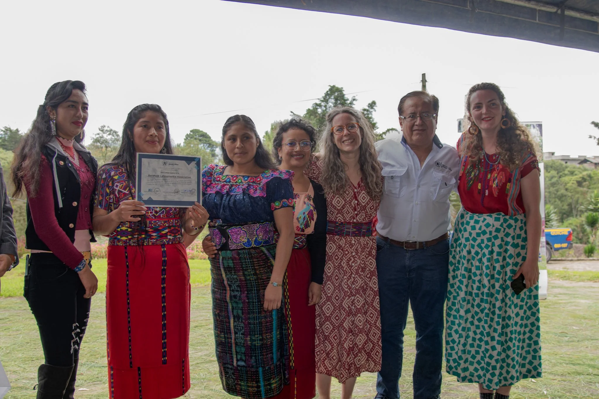 Mujer recibe reconocimiento mostrándolo con el equipo de mujeres de Barefoot College Guatemala y un hombre