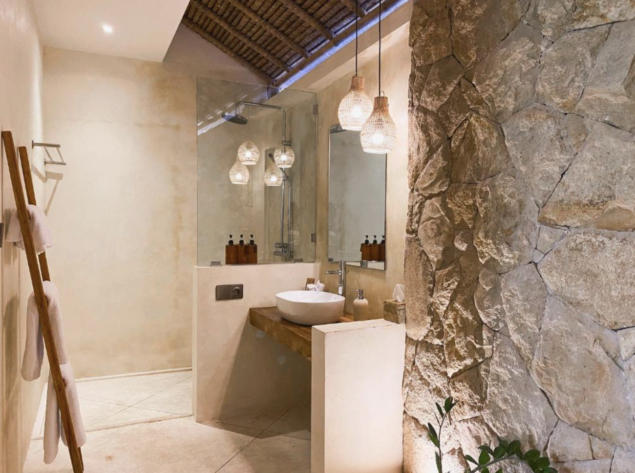 Modern rustic bathroom with stone accent wall, wooden vanity, vessel sink, large mirror, pendant lights, and a glass-enclosed shower.