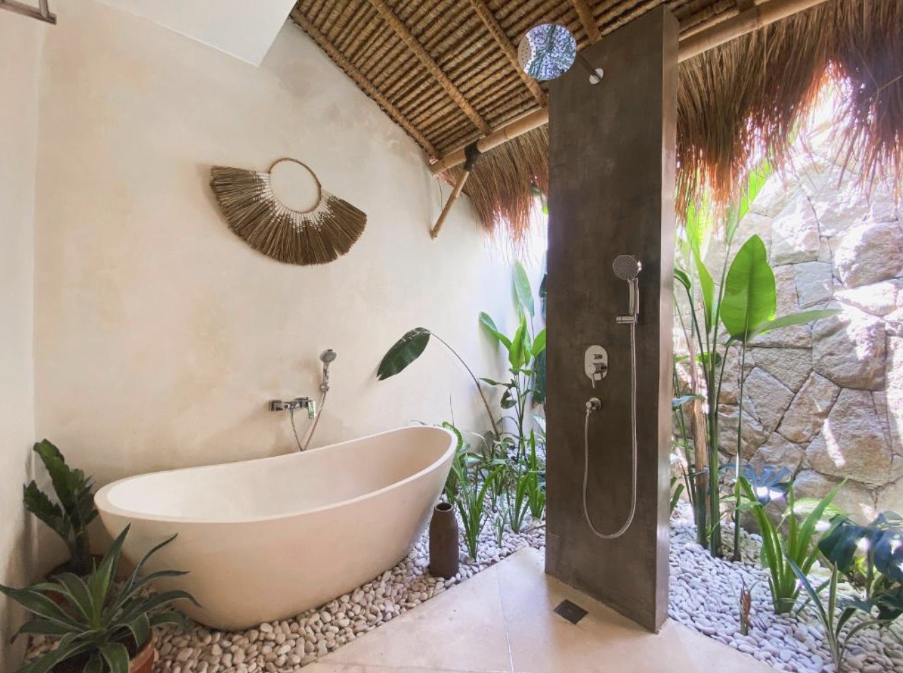 Outdoor bathroom with a freestanding bathtub, plants, a shower area, and rustic decor.
