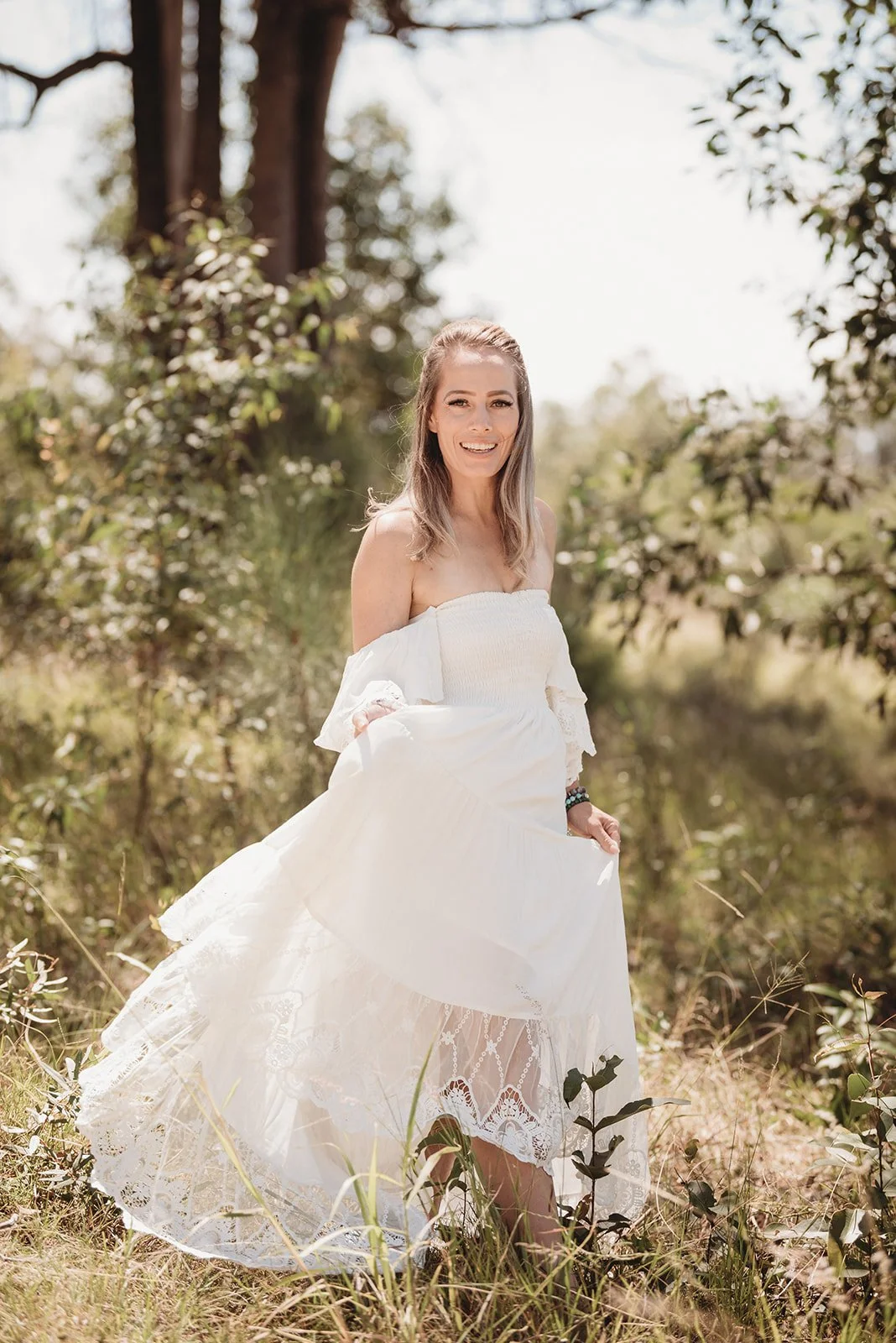 Cas in a flowing white dress in a field of green trees and long grass