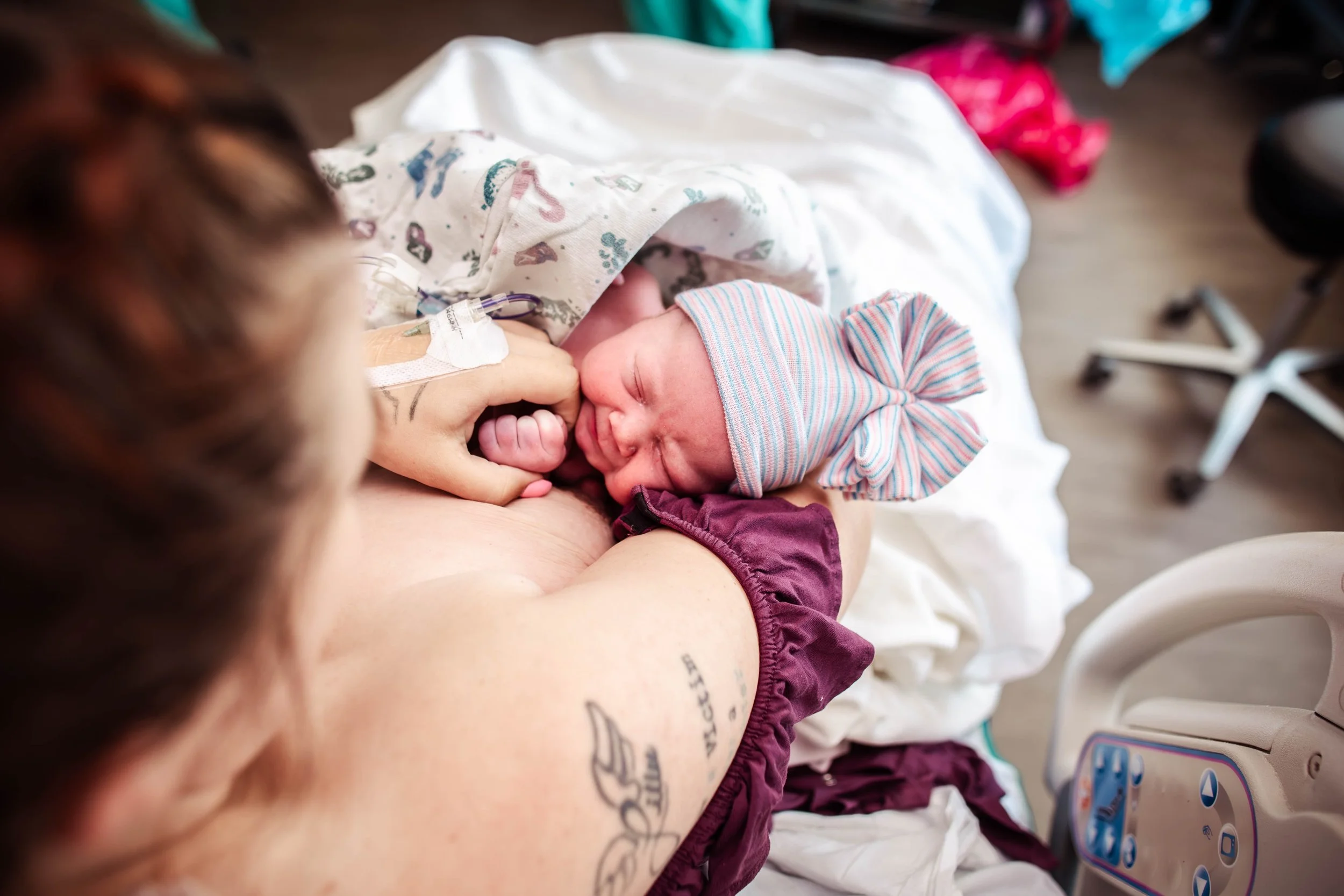 mother holding newborn in the hospital after a beautiful birth baby girl wearing bow hat wrapped in blanket on mom