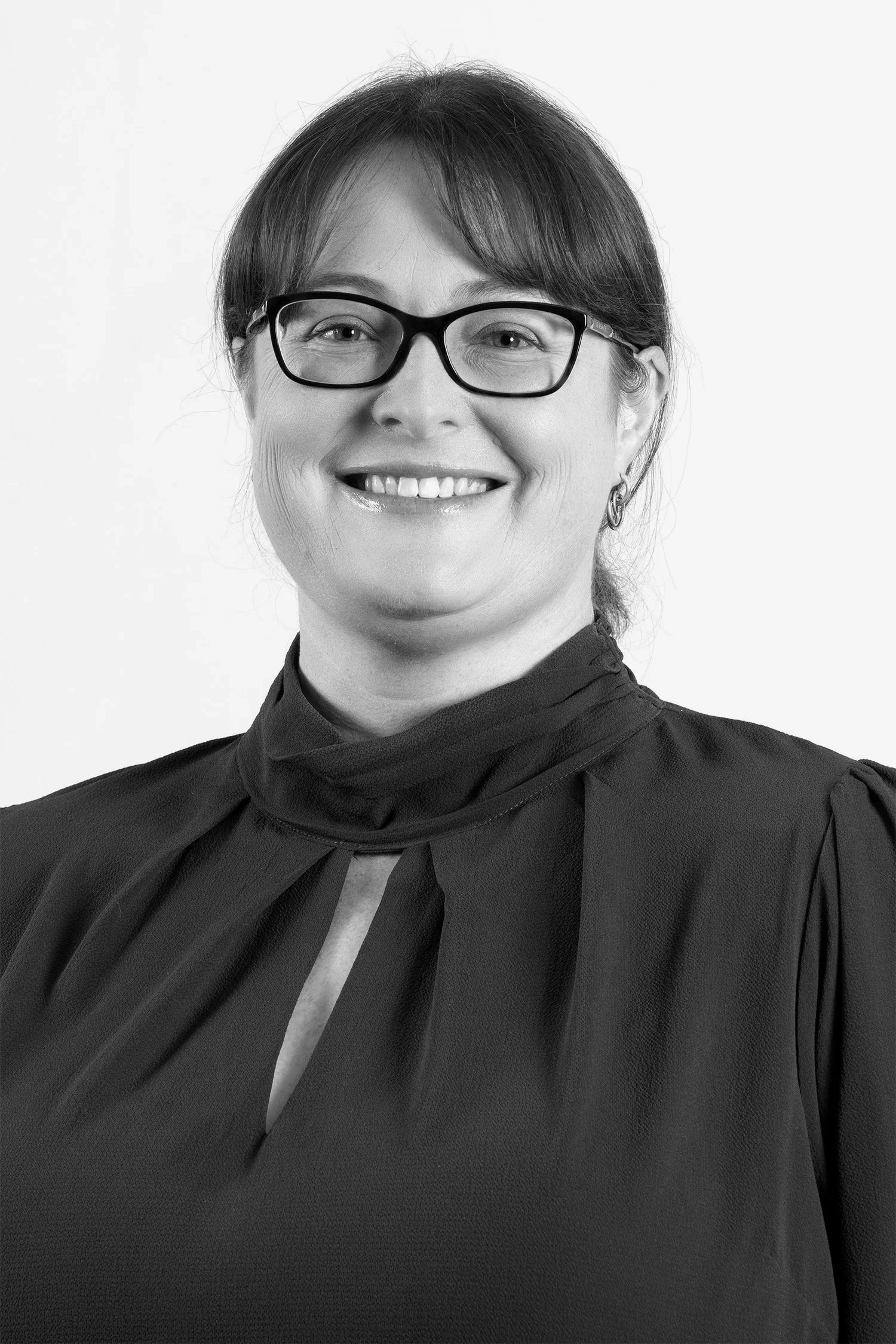 A black-and-white portrait of a woman with short hair, wearing glasses, a high-necked top, and smiling.