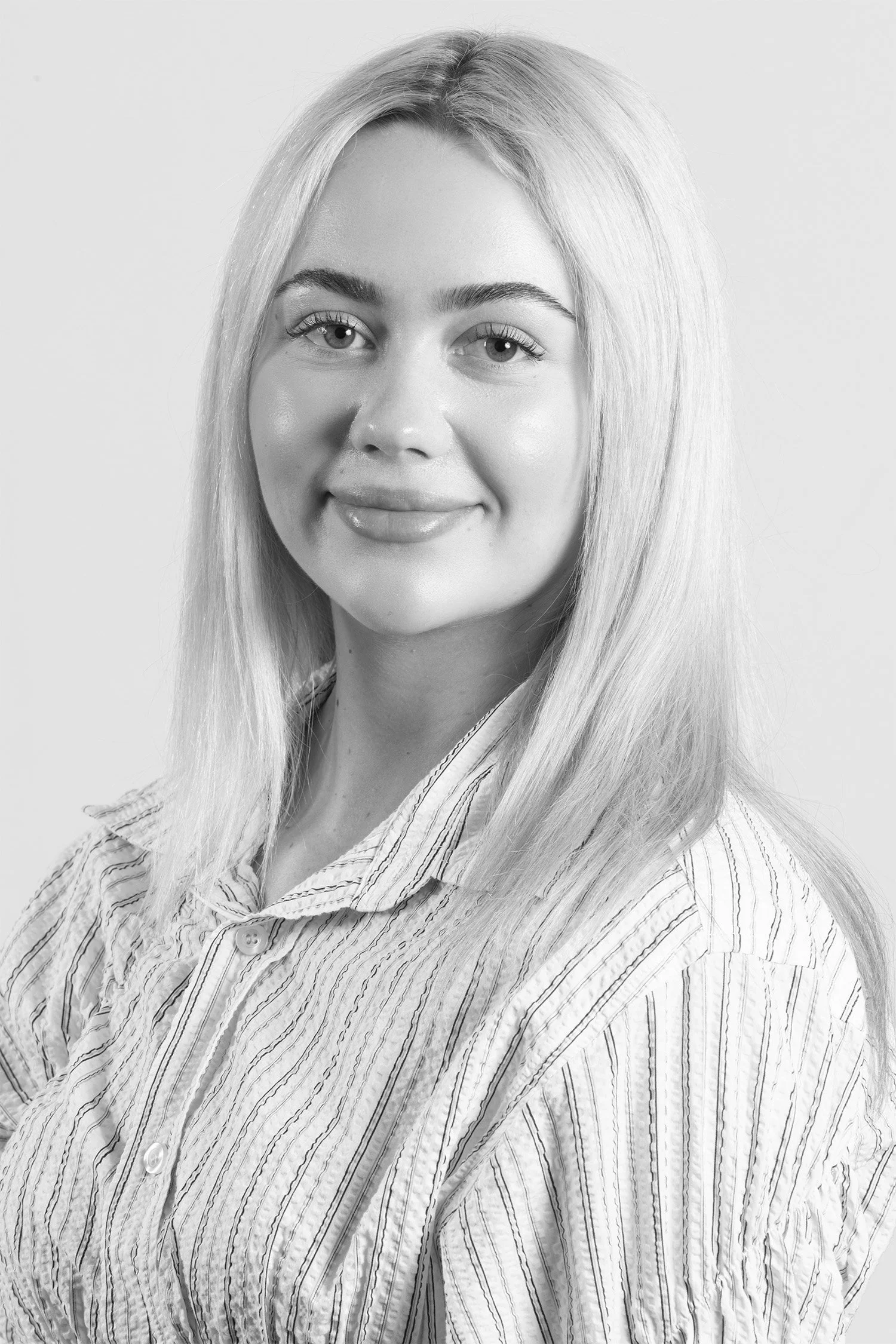 Black and white portrait of a young woman with long, straight hair, wearing a striped button-up shirt, smiling softly at the camera.