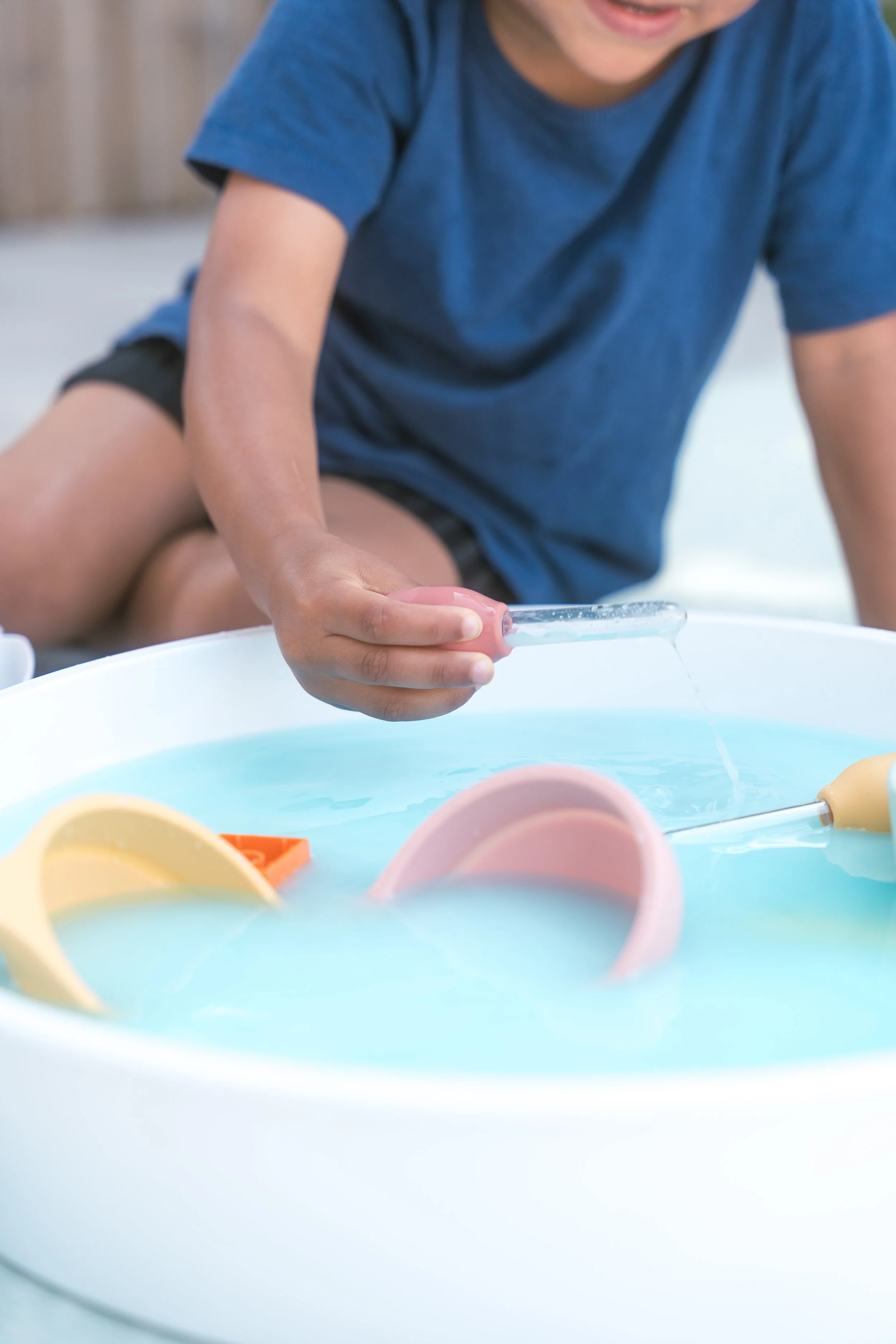 Child using sensory play dropper for colour mixing and water play