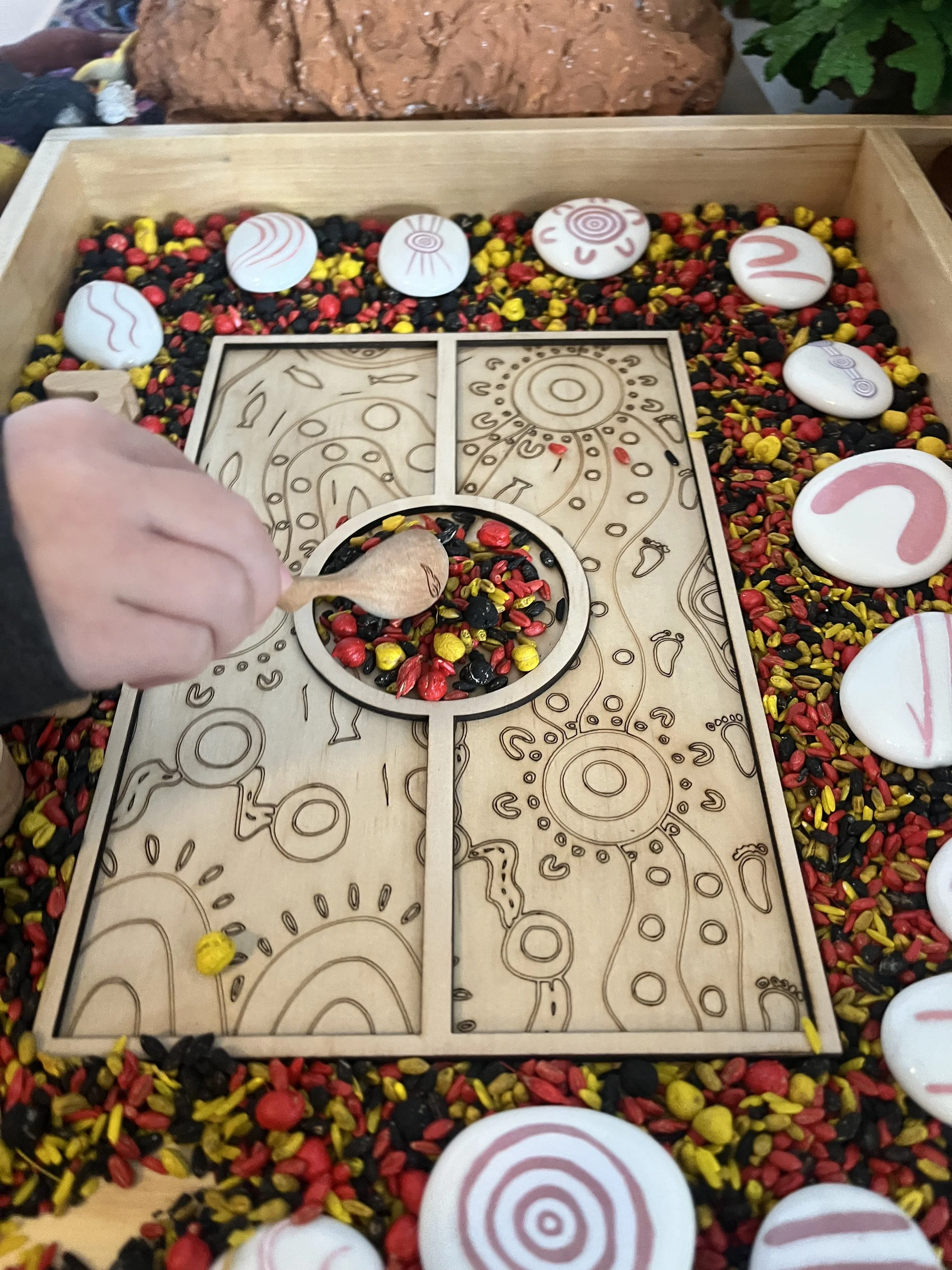 Child exploring a NAIDOC Week sensory tray with coloured rice, natural materials and Indigenous-inspired loose parts for hands-on learning.